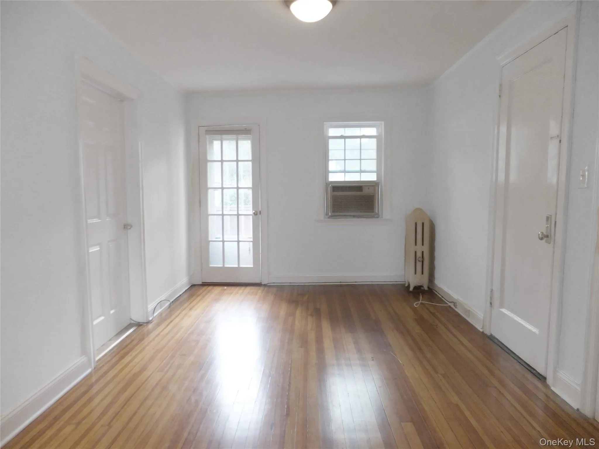 Unfurnished room with hardwood / wood-style floors, radiator heating unit, and cooling unit Unfurnished room with hardwood / wood-style floors, radiator heating unit, and cooling unit