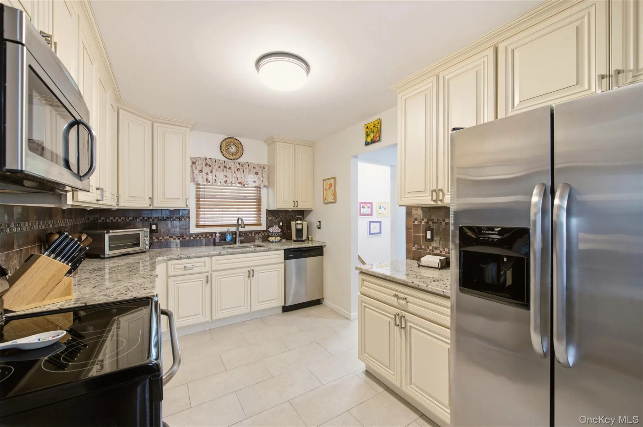 Bright and open kitchen featuring cream-colored cabinetry, stainless steel appliances, granite countertops, and a mosaic tile backsplash Bright and open kitchen featuring cream-colored cabinetry, stainless steel appliances, granite countertops, and a mosaic tile backsplash