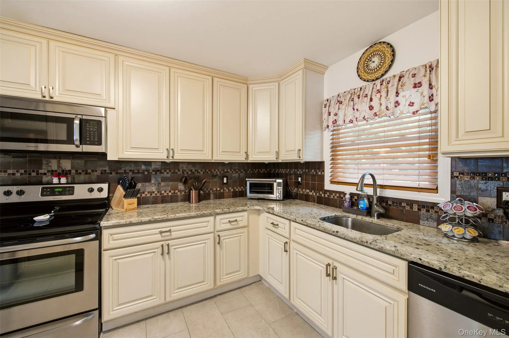 Bright and open kitchen featuring cream-colored cabinetry, stainless steel appliances, granite countertops, and a mosaic tile backsplash Bright and open kitchen featuring cream-colored cabinetry, stainless steel appliances, granite countertops, and a mosaic tile backsplash