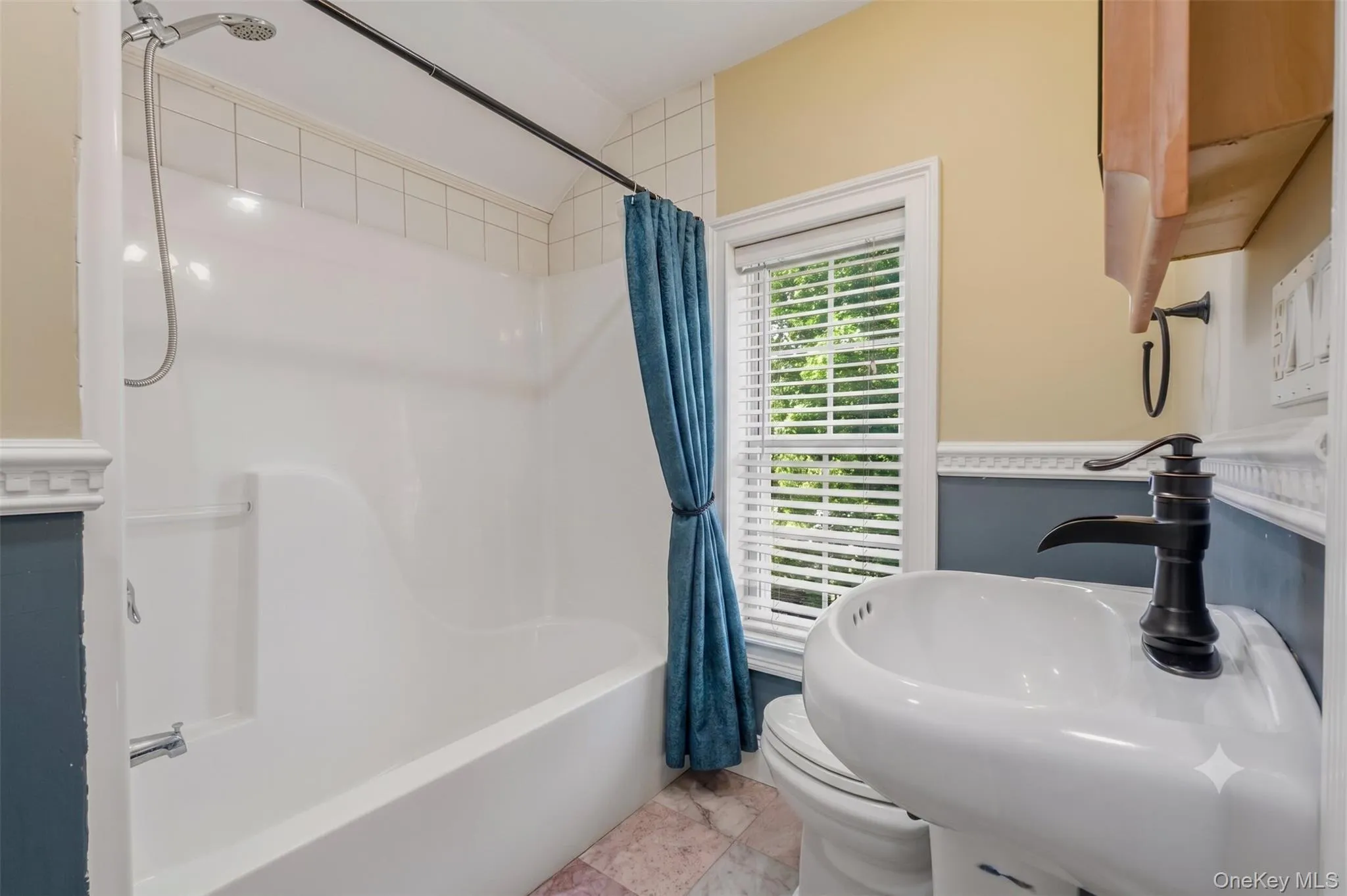 Full bathroom featuring a tub/shower combination, white surround, window with natural light, blue-and-neutral wall tones, decorative trim, and a vanity with updated faucet. Full bathroom featuring a tub/shower combination, white surround, window with natural light, blue-and-neutral wall tones, decorative trim, and a vanity with updated faucet.