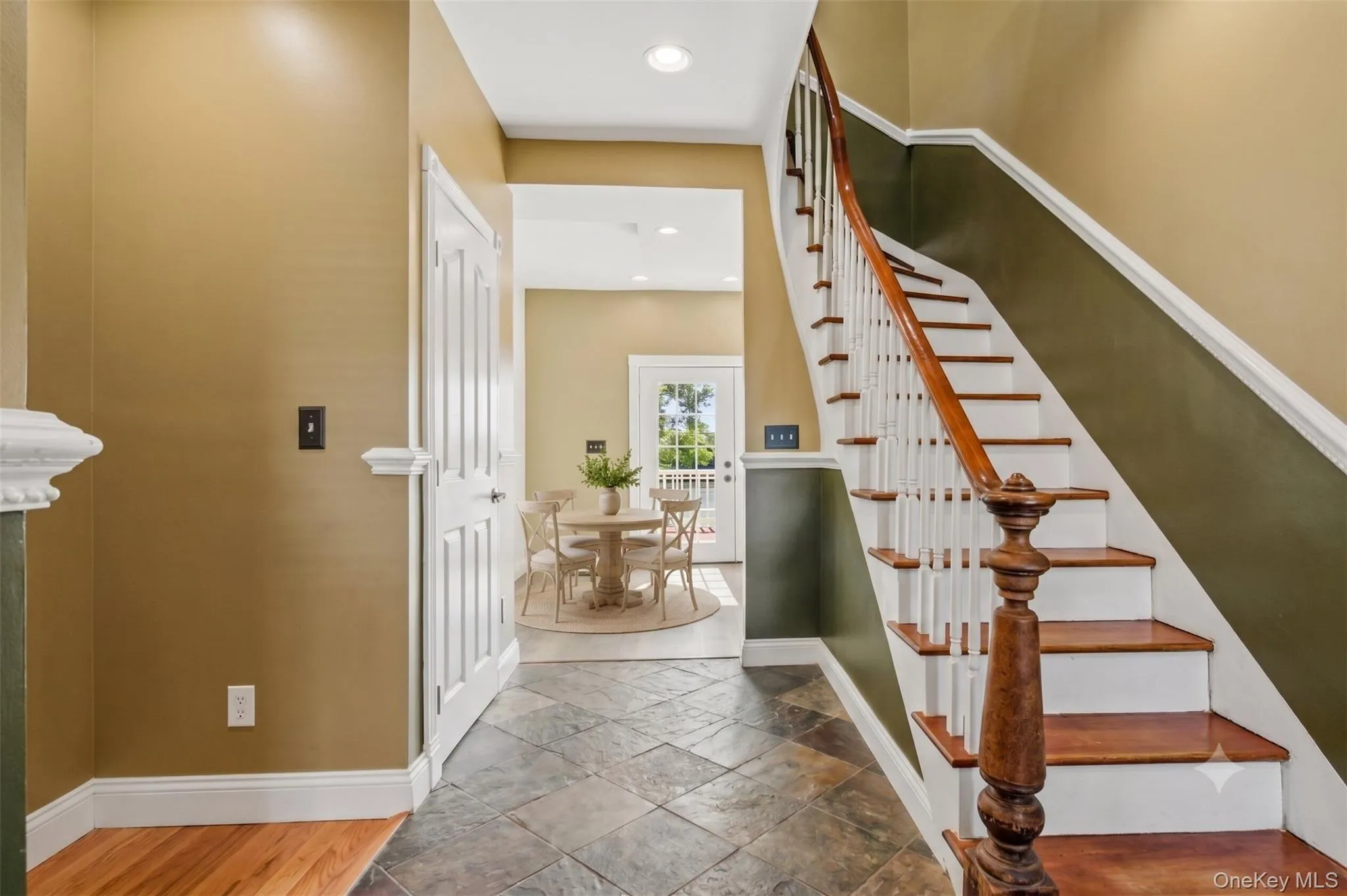 Virtually Staged. Welcoming foyer featuring slate-style tile flooring, classic staircase with wood treads, white spindles, detailed trim, and warm two-tone wall accents that add character to the home. Virtually Staged. Welcoming foyer featuring slate-style tile flooring, classic staircase with wood treads, white spindles, detailed trim, and warm two-tone wall accents that add character to the home.