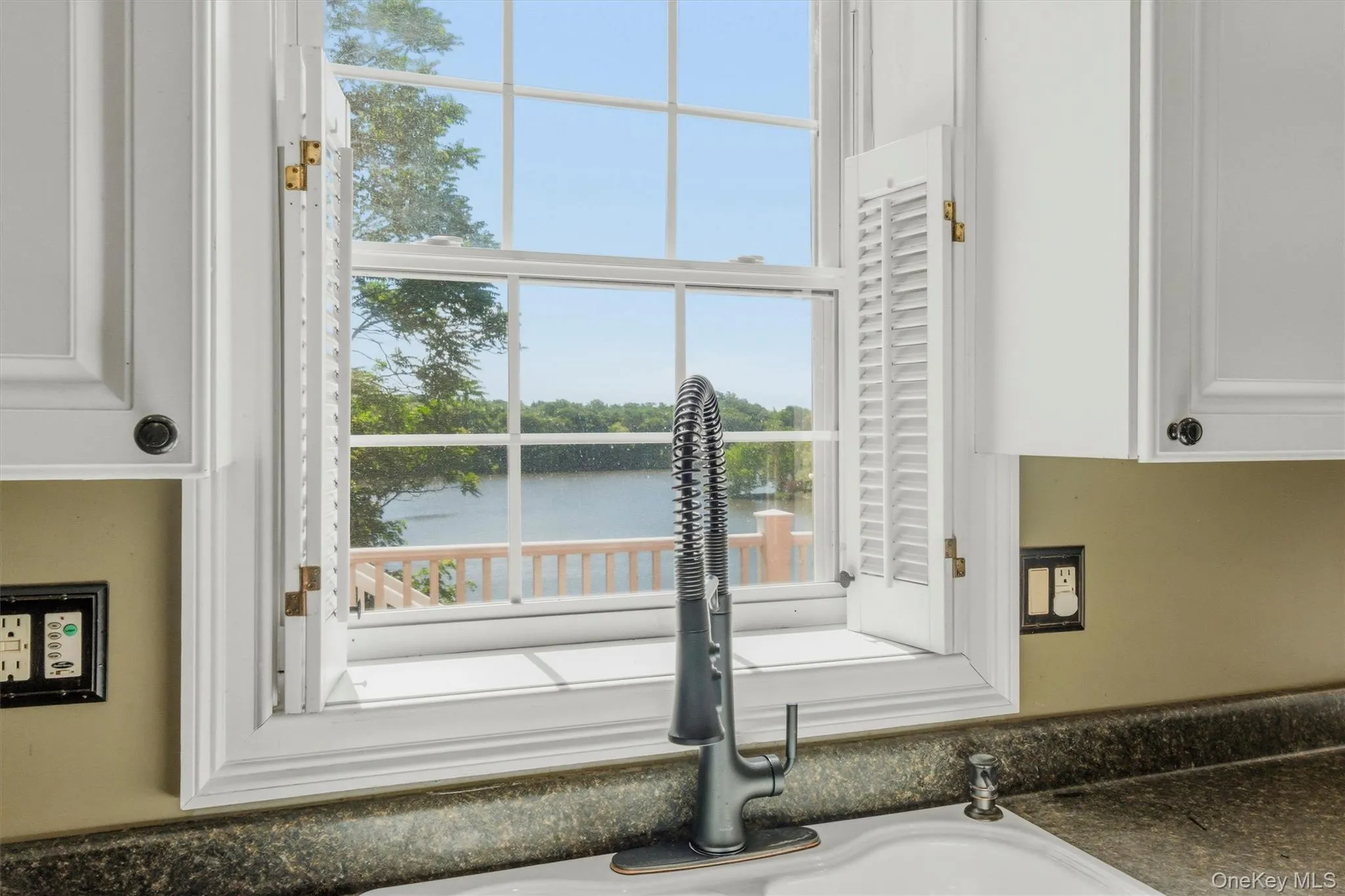 Kitchen detail highlighting the bright window over the sink, updated faucet, white cabinetry, and scenic water view, adding charm and everyday appeal to the kitchen space. Kitchen detail highlighting the bright window over the sink, updated faucet, white cabinetry, and scenic water view, adding charm and everyday appeal to the kitchen space.