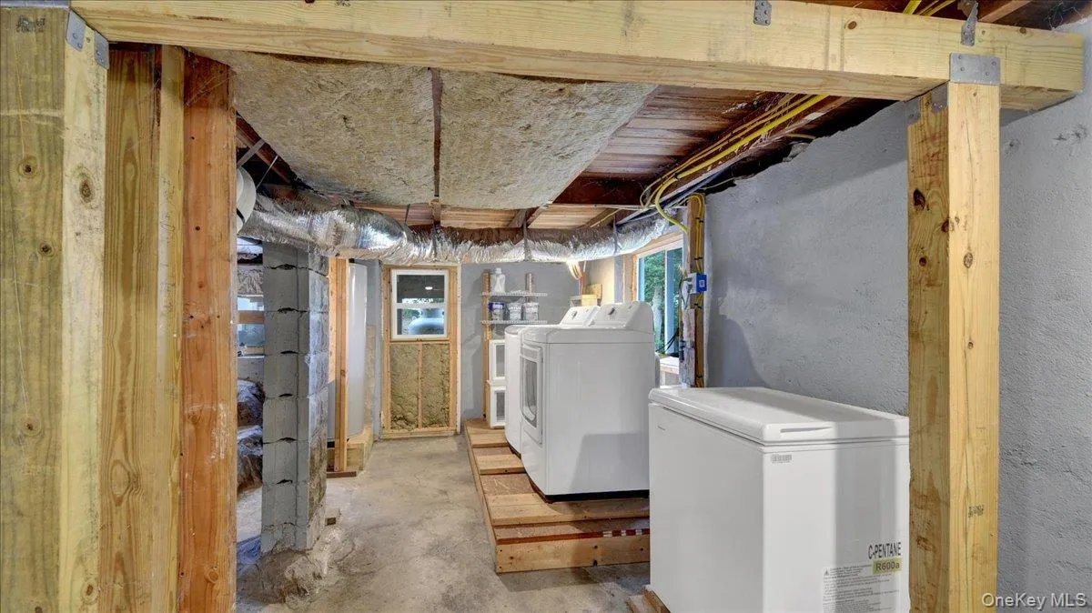 Utility room featuring exposed wooden structural beams, concrete block walls, and a concrete floor Utility room featuring exposed wooden structural beams, concrete block walls, and a concrete floor