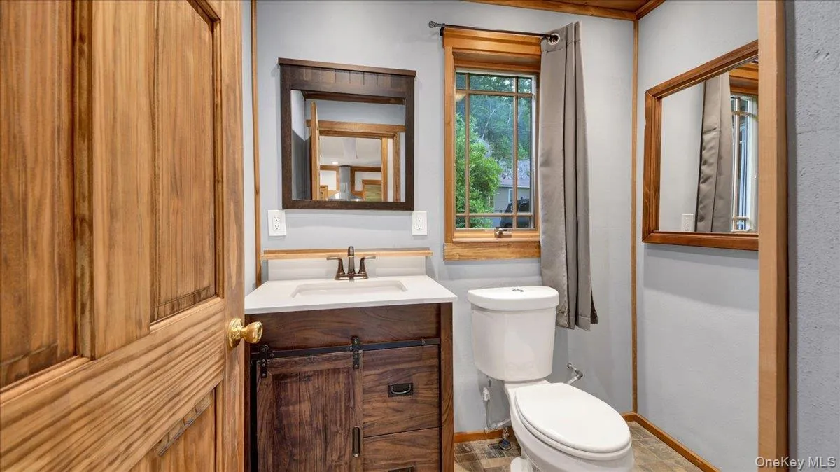 Bathroom featuring a wood-finish vanity with a white countertop and rectangular undermount sink, a bronze-finish faucet, and a wall-mounted mirror Bathroom featuring a wood-finish vanity with a white countertop and rectangular undermount sink, a bronze-finish faucet, and a wall-mounted mirror