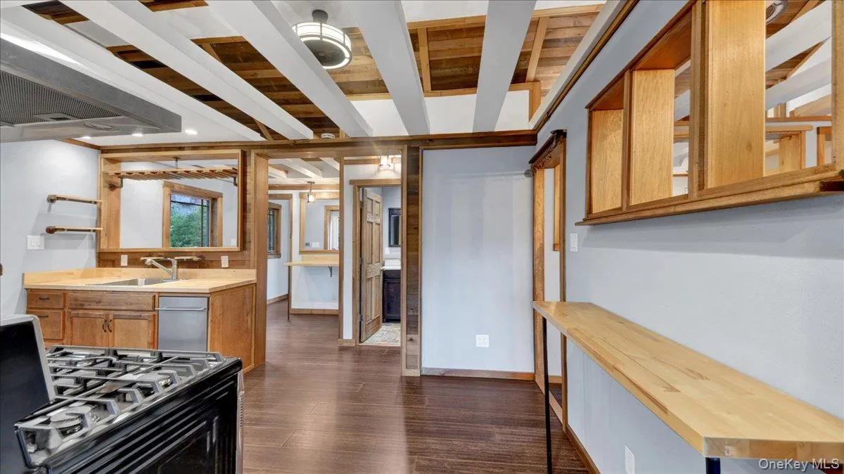 Kitchen and dining area featuring wood-finish flooring, exposed wood beam ceiling with white accents, wood cabinetry, built-in shelving, and a stainless steel dishwasher Kitchen and dining area featuring wood-finish flooring, exposed wood beam ceiling with white accents, wood cabinetry, built-in shelving, and a stainless steel dishwasher