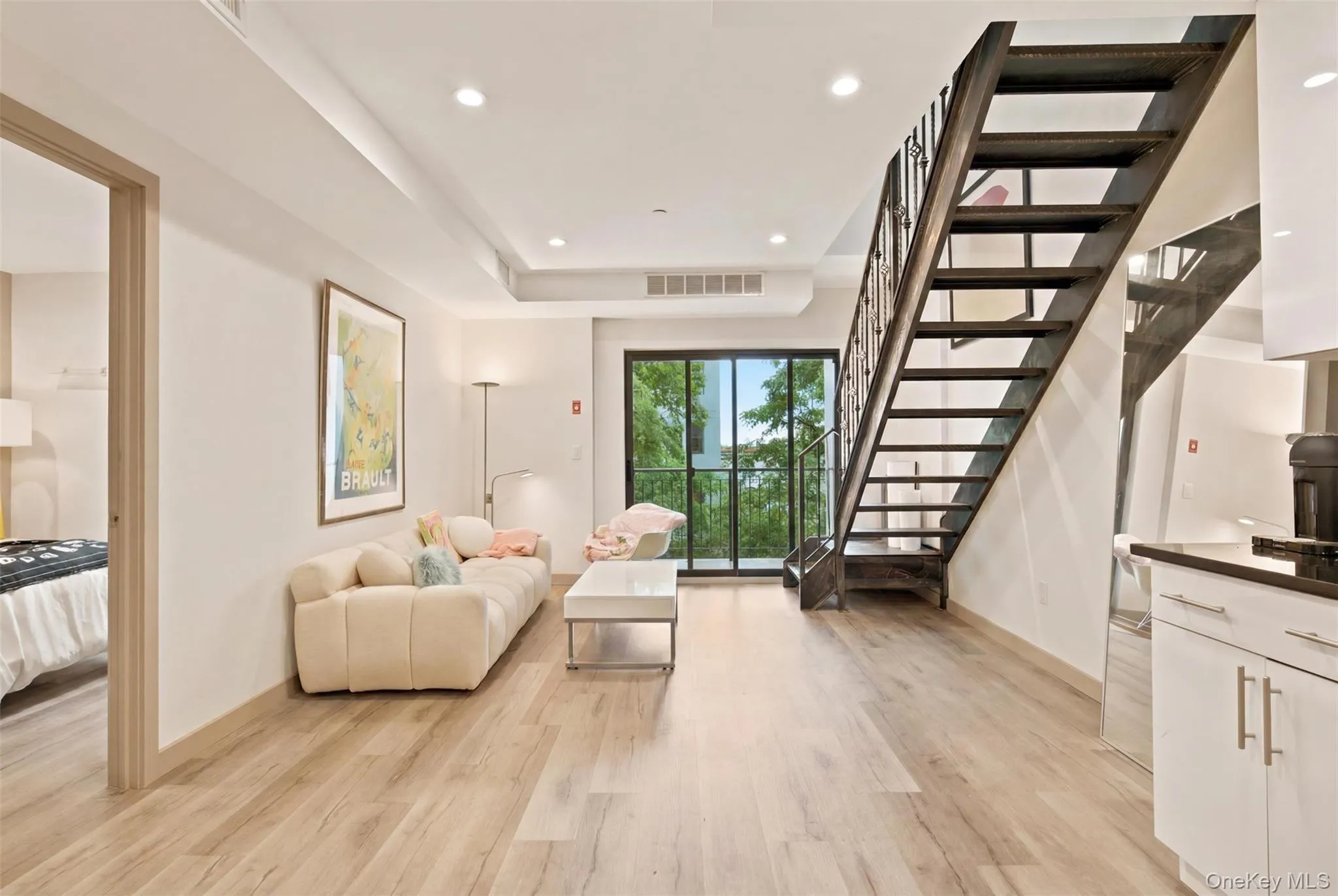 Open-concept living space featuring wood-finish flooring, recessed lighting, and a modern dark wood staircase with metal balusters Open-concept living space featuring wood-finish flooring, recessed lighting, and a modern dark wood staircase with metal balusters