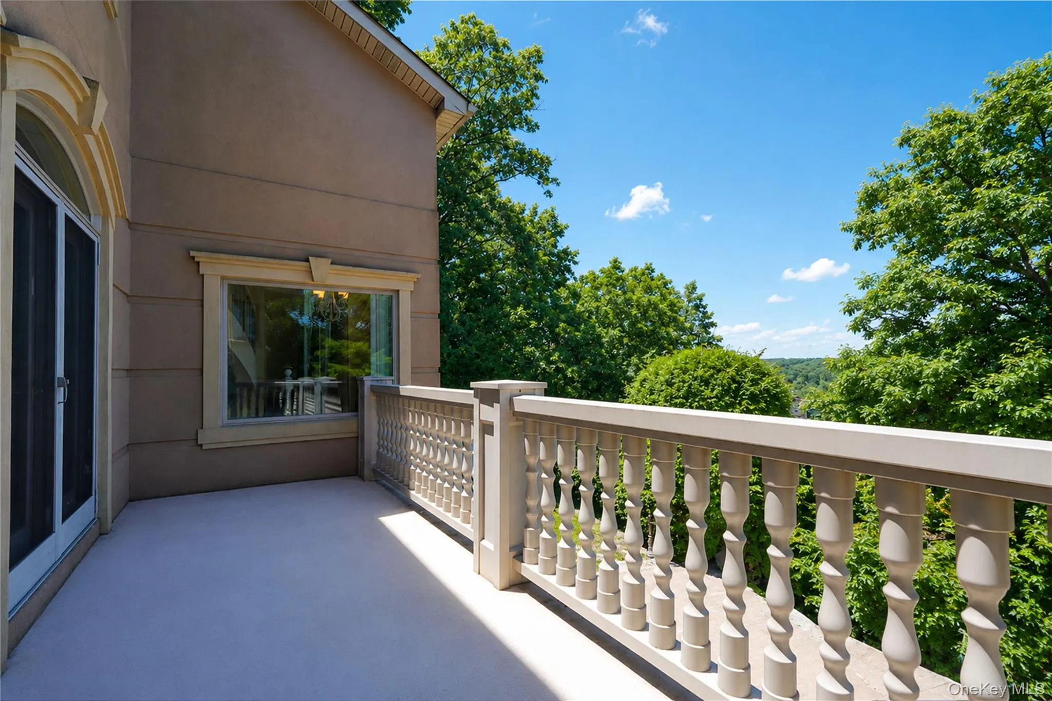 Outdoor balcony featuring light-toned flooring, ornate balusters, a large arch-top door, and a rectangular window with decorative trim Outdoor balcony featuring light-toned flooring, ornate balusters, a large arch-top door, and a rectangular window with decorative trim