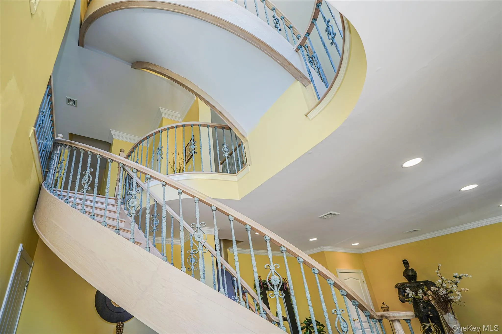 Curving staircase featuring decorative wrought iron balusters, wood-finish handrails, and a grand two-story ceiling Curving staircase featuring decorative wrought iron balusters, wood-finish handrails, and a grand two-story ceiling
