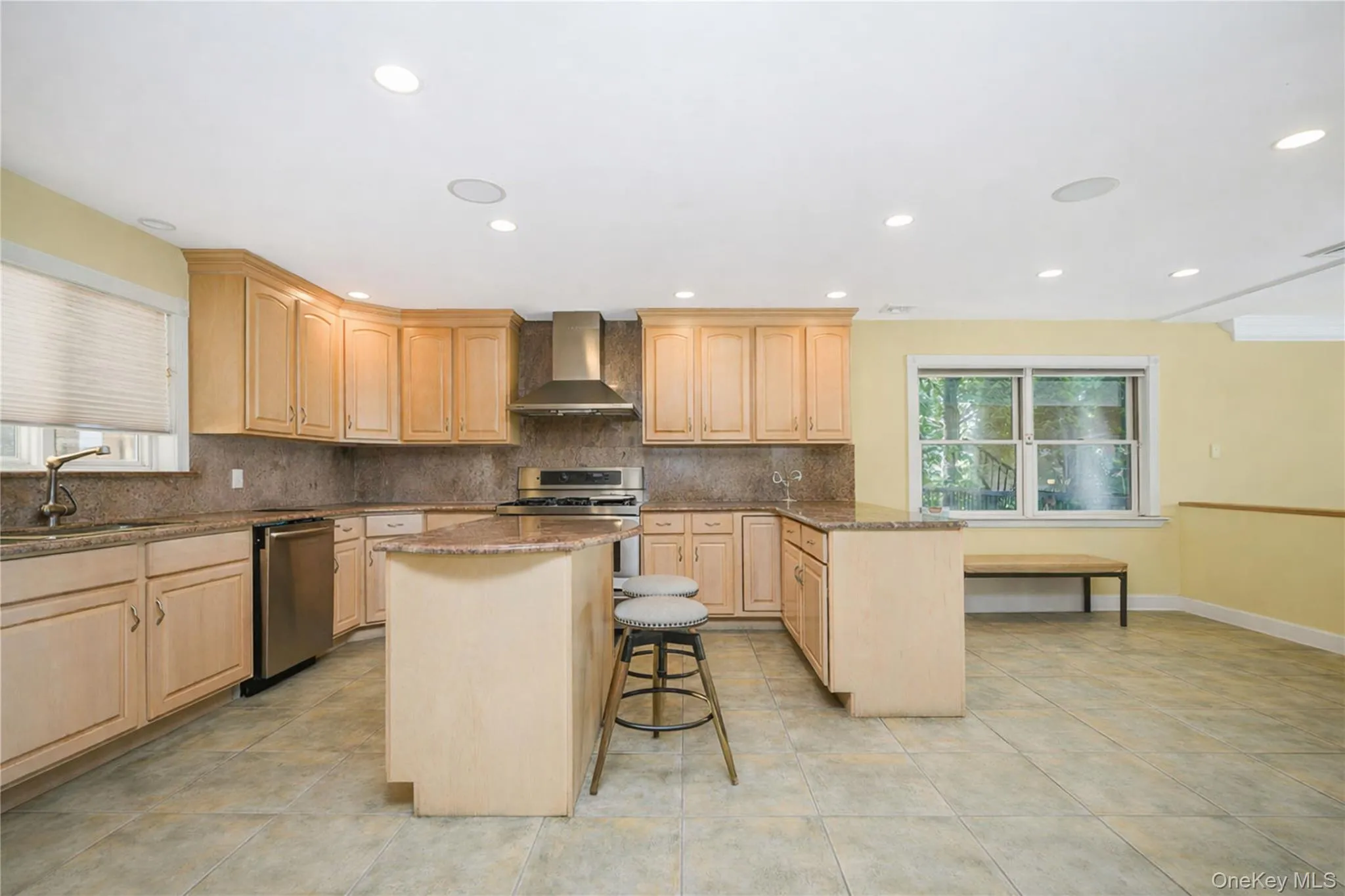 Spacious kitchen featuring light wood cabinetry, stone countertops, stainless steel appliances, and a central island with bar seating Spacious kitchen featuring light wood cabinetry, stone countertops, stainless steel appliances, and a central island with bar seating