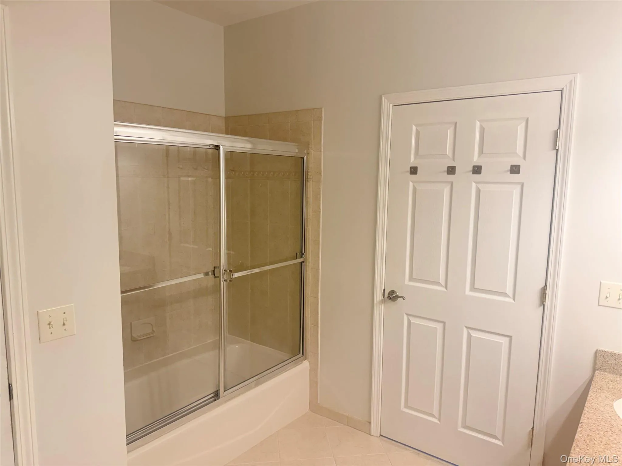 Bathroom featuring a bathtub with a sliding glass enclosure, tile surround, and a four-panel door with decorative hooks Bathroom featuring a bathtub with a sliding glass enclosure, tile surround, and a four-panel door with decorative hooks