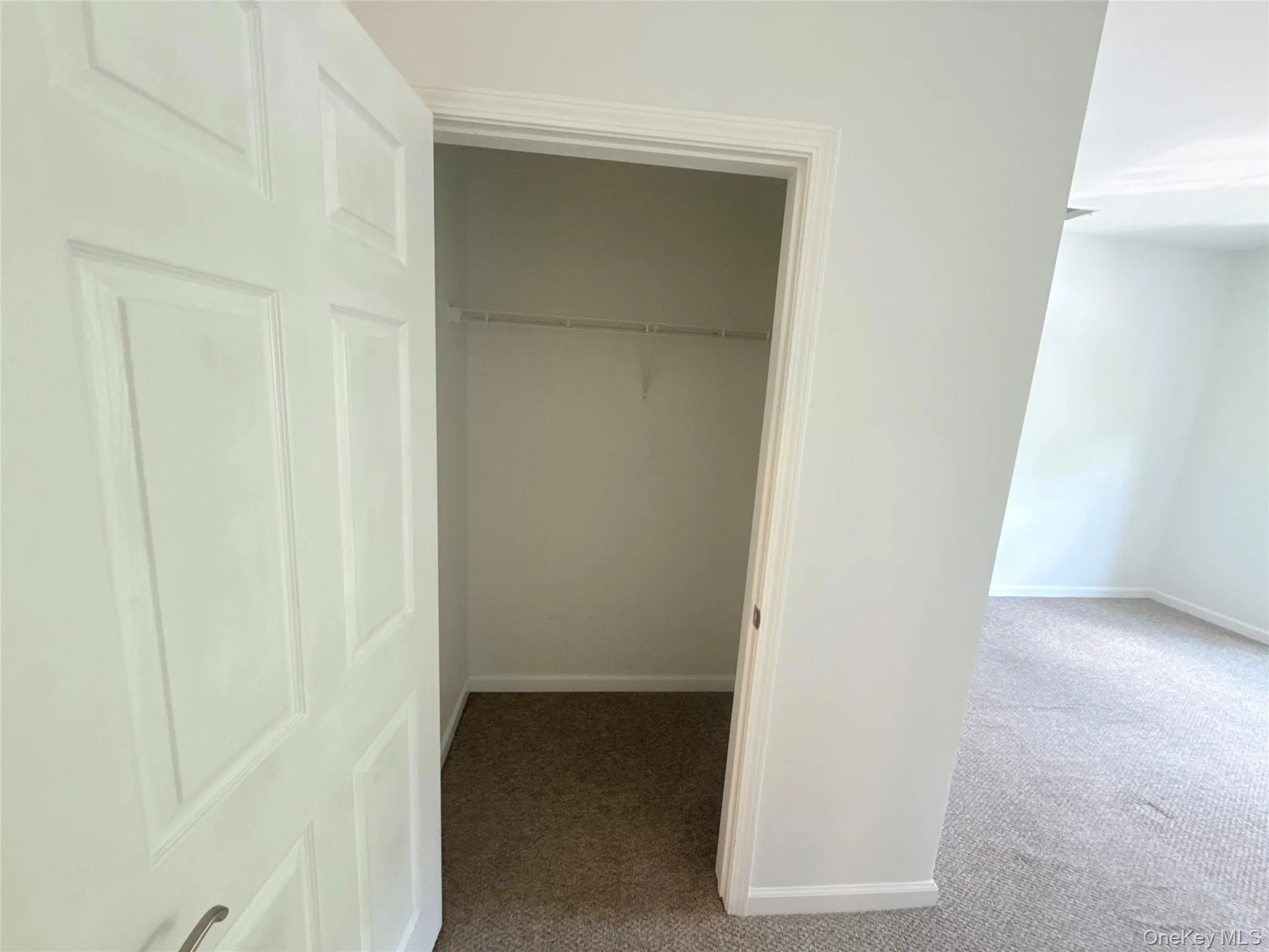Closet space featuring a built-in wire shelf and rod, complemented by neutral carpeting and white trim Closet space featuring a built-in wire shelf and rod, complemented by neutral carpeting and white trim