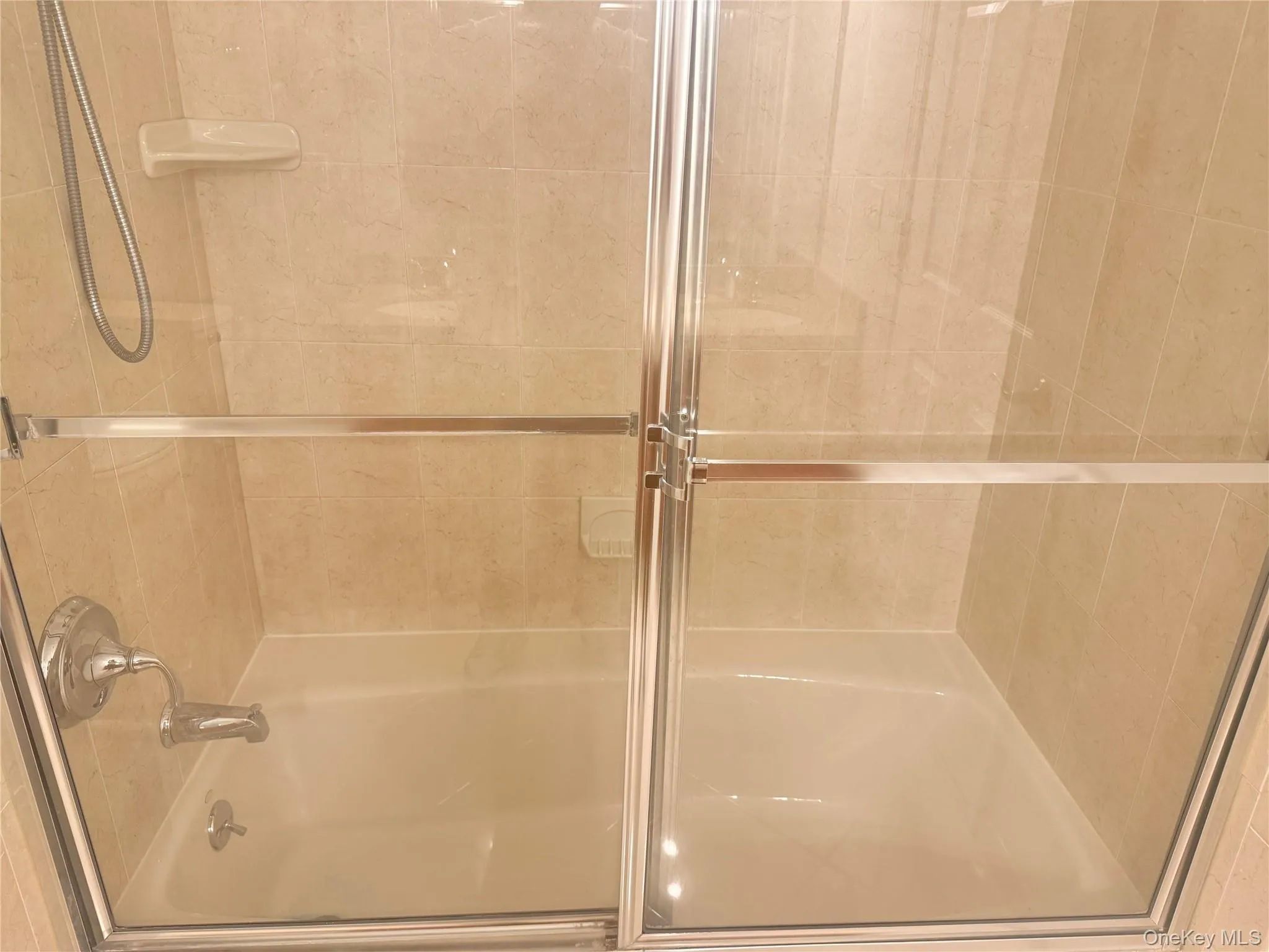 Bathtub and shower combination featuring neutral-toned wall tiling, chrome fixtures, and a clear glass shower enclosure with a sliding door Bathtub and shower combination featuring neutral-toned wall tiling, chrome fixtures, and a clear glass shower enclosure with a sliding door