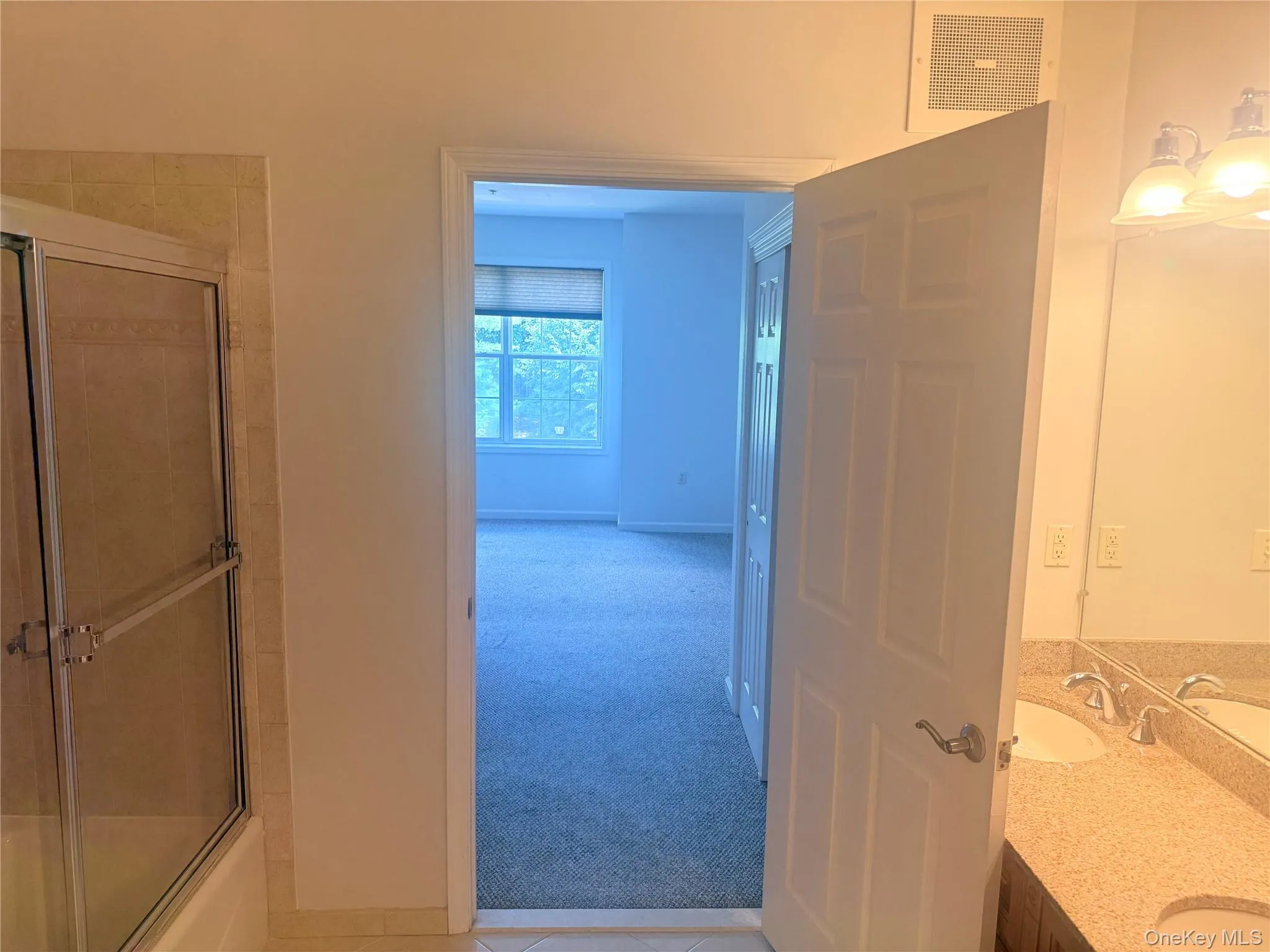 Bathroom featuring a shower with glass enclosure, dual vanity with light-toned countertop, and mirror Bathroom featuring a shower with glass enclosure, dual vanity with light-toned countertop, and mirror
