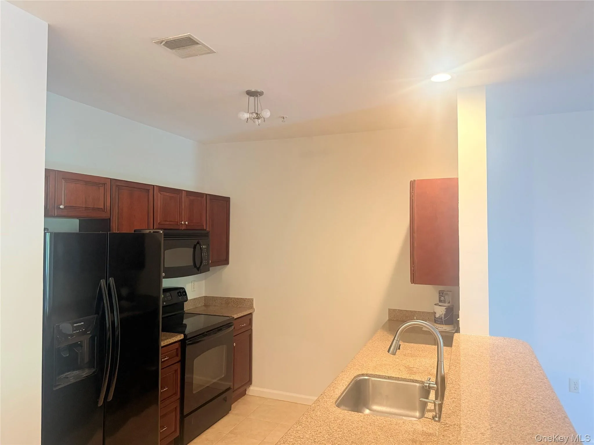 Kitchen featuring dark wood-finish cabinetry, black appliances including a refrigerator and range, and light-colored countertops Kitchen featuring dark wood-finish cabinetry, black appliances including a refrigerator and range, and light-colored countertops