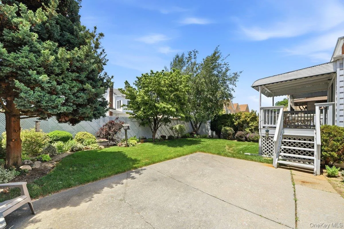 Manicured backyard with concrete patio, lush lawn, mature trees, and a covered porch with white railings and lattice detailing Manicured backyard with concrete patio, lush lawn, mature trees, and a covered porch with white railings and lattice detailing