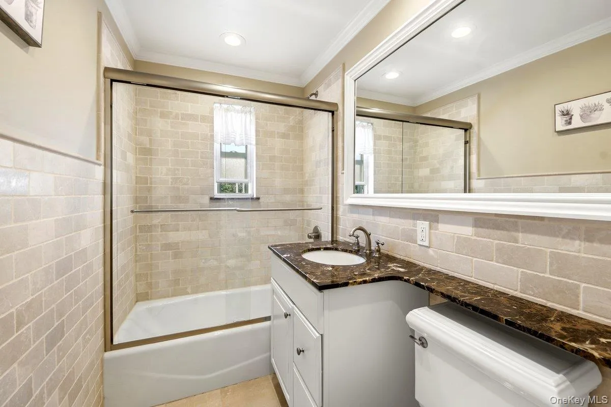 1st fl Bathroom featuring a tiled tub-shower combination with sliding glass doors, a vanity with a dark marbled countertop and an integrated sink, a large framed mirror, and recessed lighting 1st fl Bathroom featuring a tiled tub-shower combination with sliding glass doors, a vanity with a dark marbled countertop and an integrated sink, a large framed mirror, and recessed lighting
