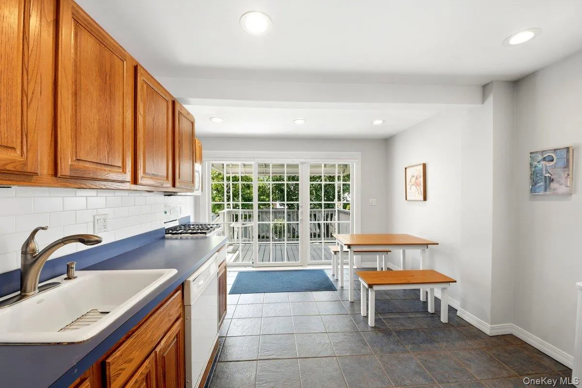 Kitchen featuring wood cabinetry, white subway tile backsplash, dark blue countertops, a built-in sink, & sliding glass door Kitchen featuring wood cabinetry, white subway tile backsplash, dark blue countertops, a built-in sink, & sliding glass door