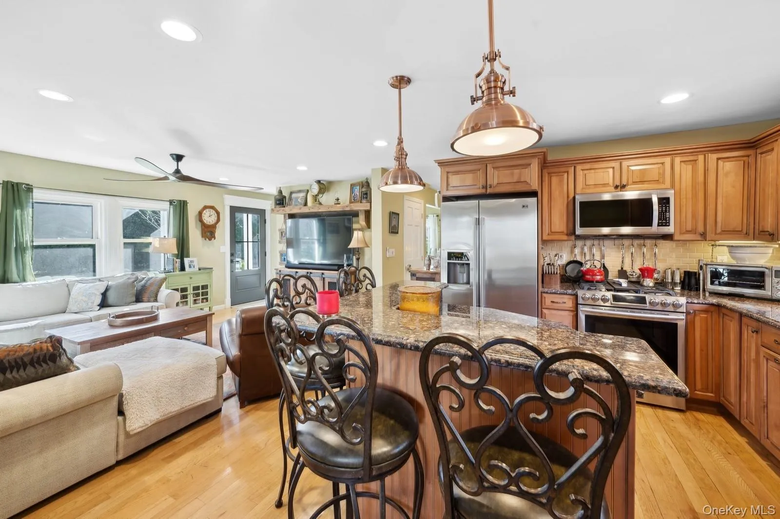 Kitchen with decorative light fixtures, light wood-type flooring, appliances with stainless steel finishes, and dark stone counters Kitchen with decorative light fixtures, light wood-type flooring, appliances with stainless steel finishes, and dark stone counters