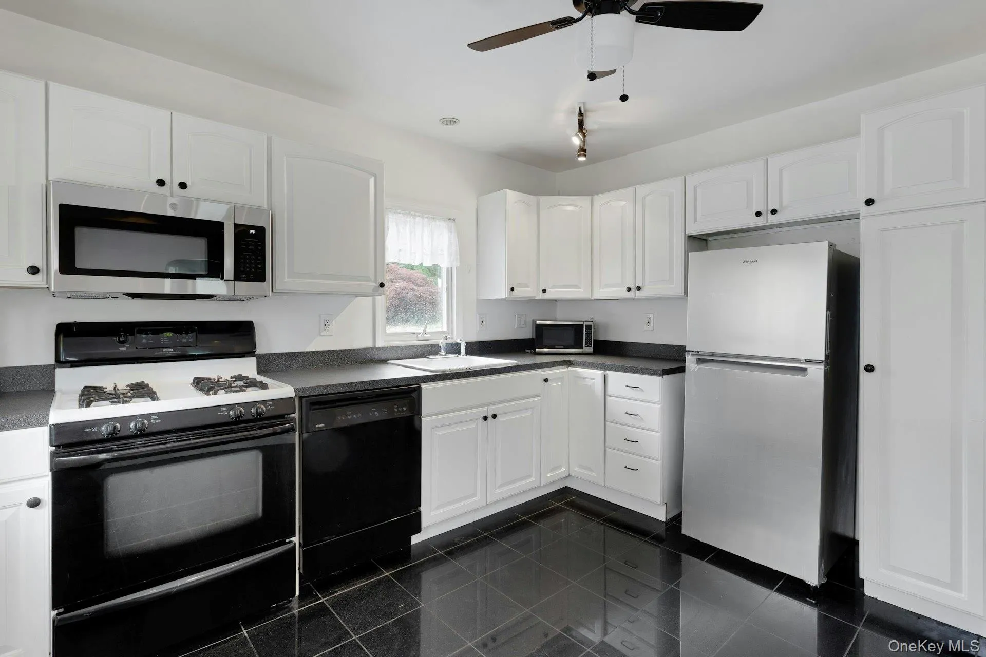 Kitchen featuring white cabinetry, black countertops, and dark tile flooring Kitchen featuring white cabinetry, black countertops, and dark tile flooring