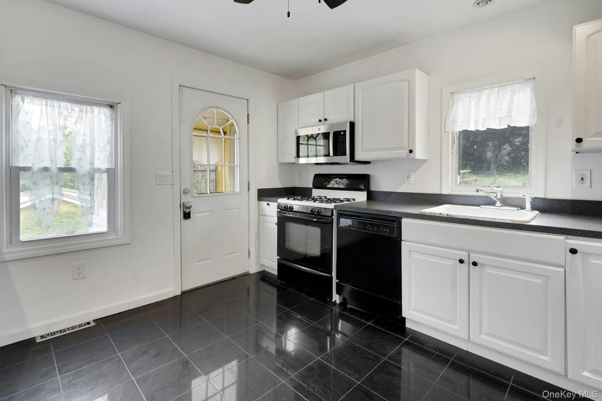 Kitchen featuring black tile flooring, white cabinetry, black countertops, and stainless steel appliances Kitchen featuring black tile flooring, white cabinetry, black countertops, and stainless steel appliances