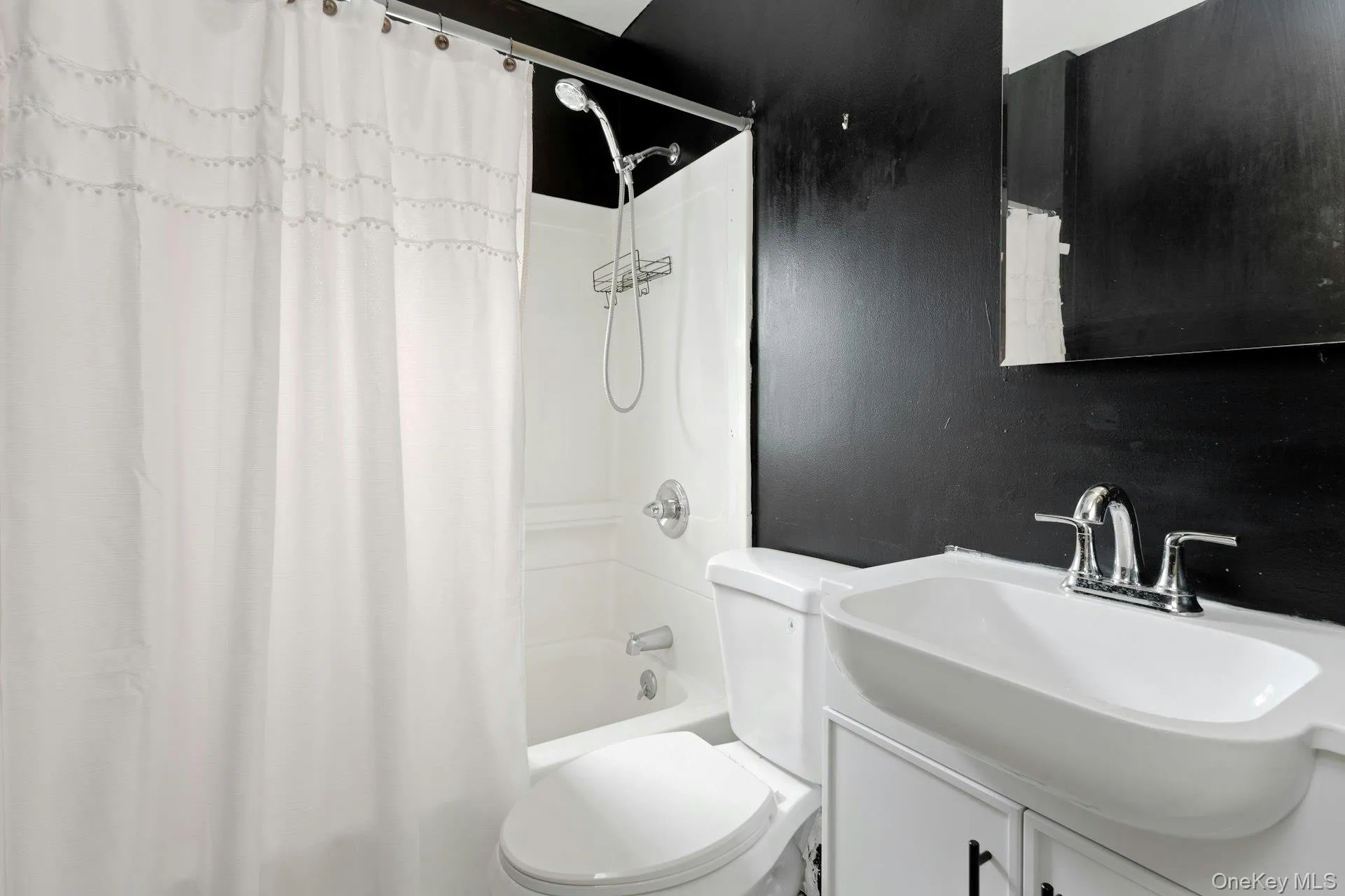 Bathroom featuring a white bathtub and shower combination, a white toilet, and a white vanity with an integrated rectangular sink Bathroom featuring a white bathtub and shower combination, a white toilet, and a white vanity with an integrated rectangular sink