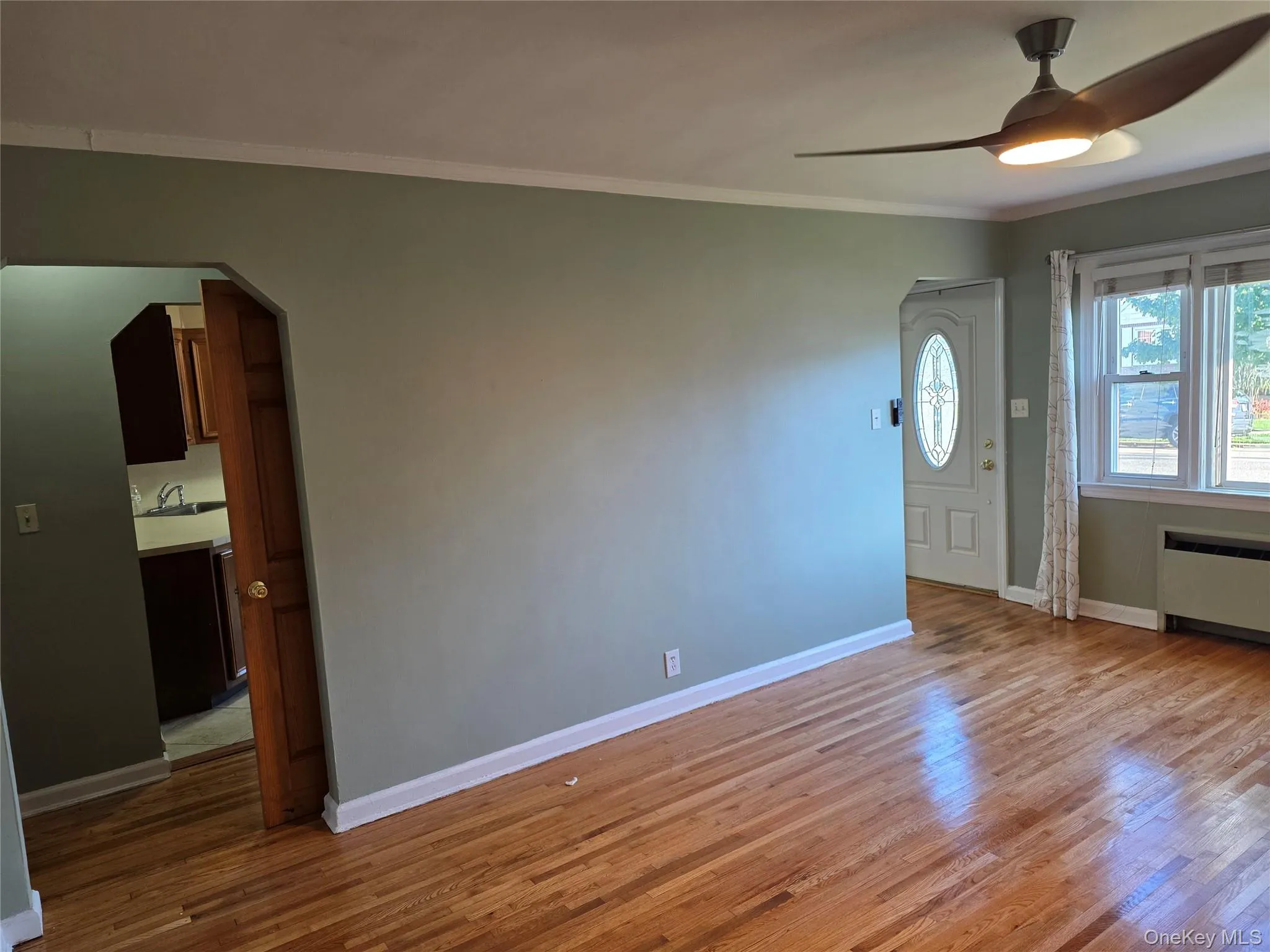 Entrance foyer featuring wood finished floors, ornamental molding, a ceiling fan, arched walkways, and radiator Entrance foyer featuring wood finished floors, ornamental molding, a ceiling fan, arched walkways, and radiator