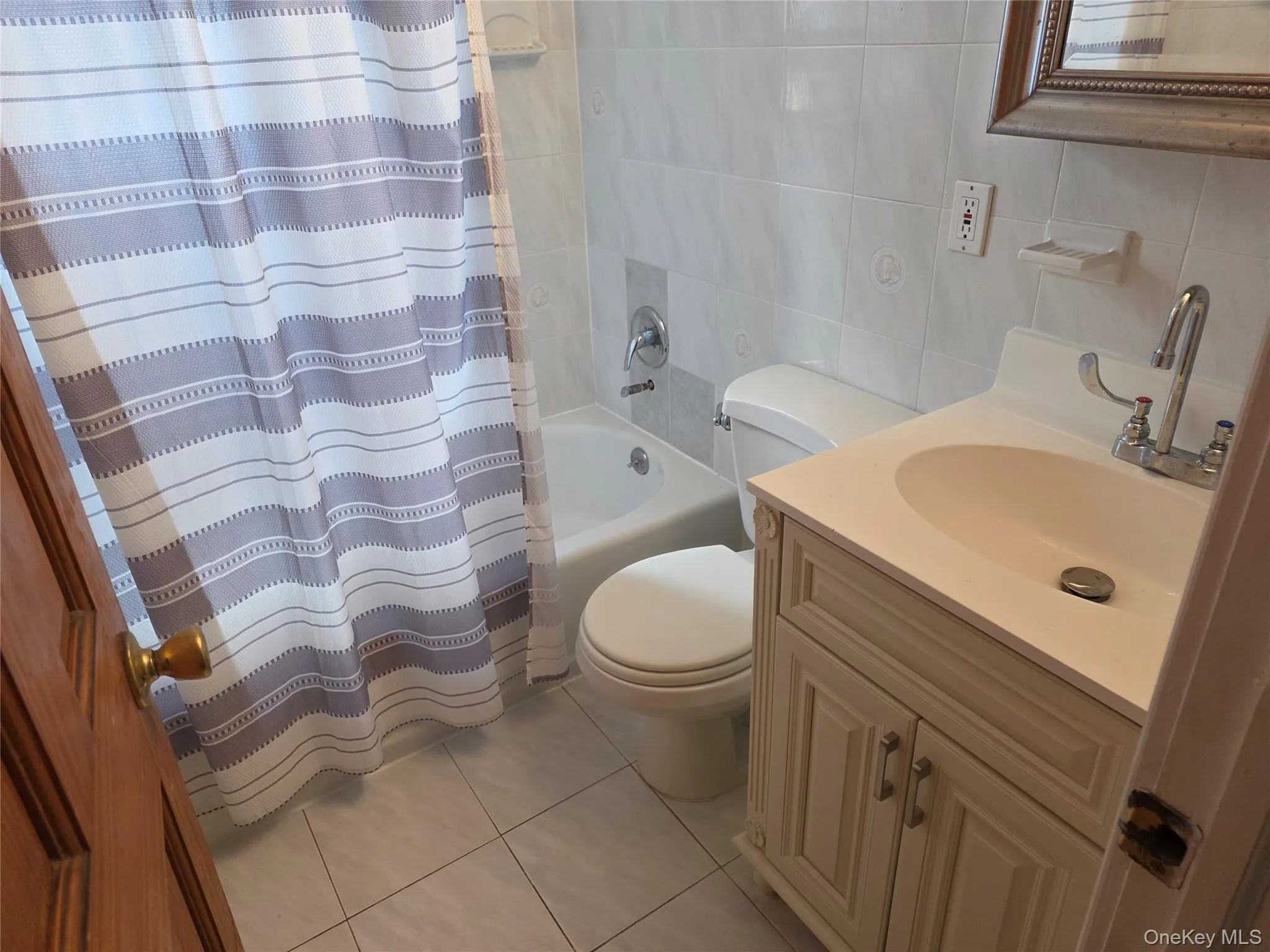 Full bathroom with tile walls, light tile patterned floors, vanity, and shower / tub combo Full bathroom with tile walls, light tile patterned floors, vanity, and shower / tub combo