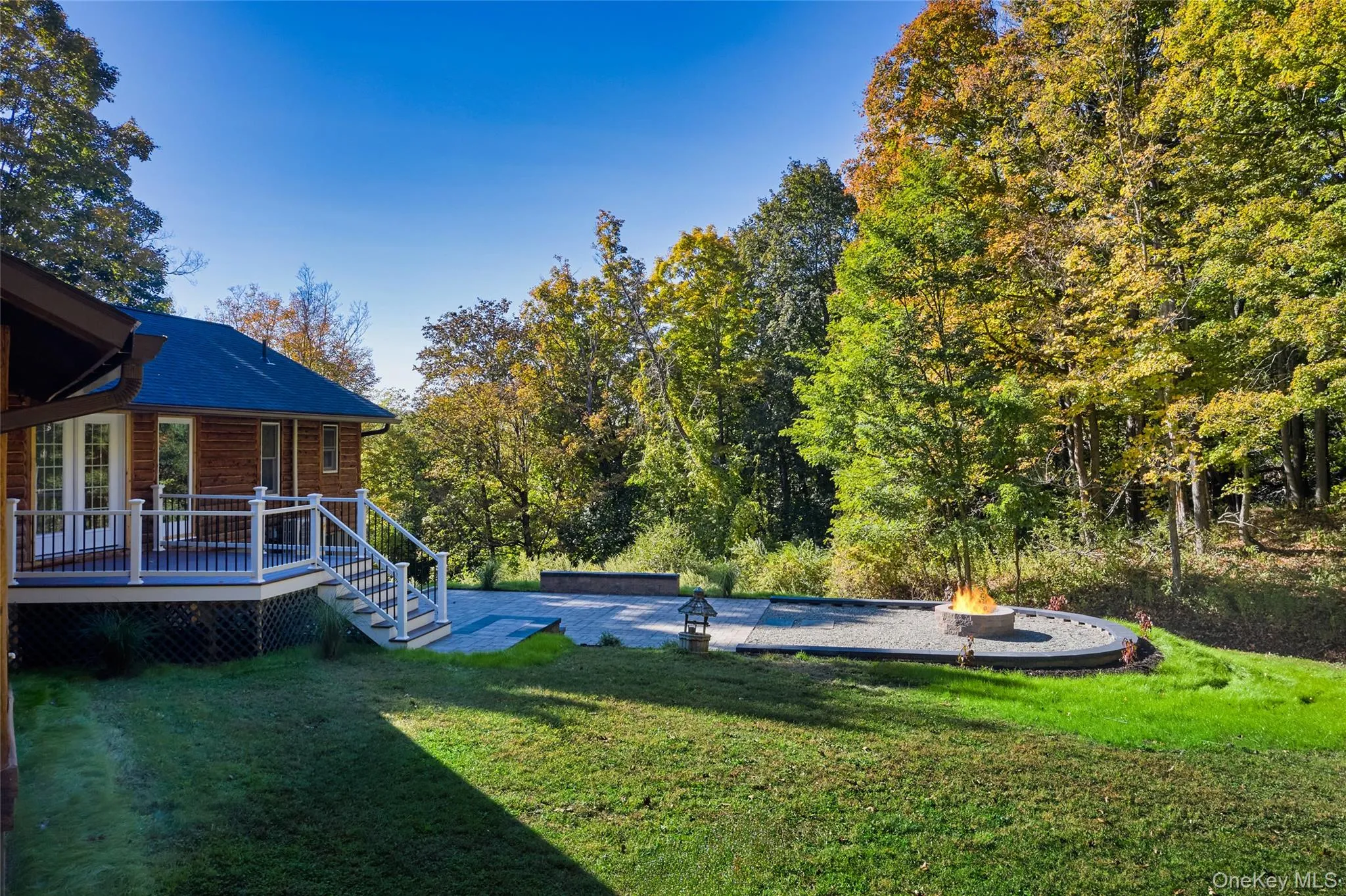View of grassy yard featuring an outdoor fire pit, a patio area, and a deck View of grassy yard featuring an outdoor fire pit, a patio area, and a deck