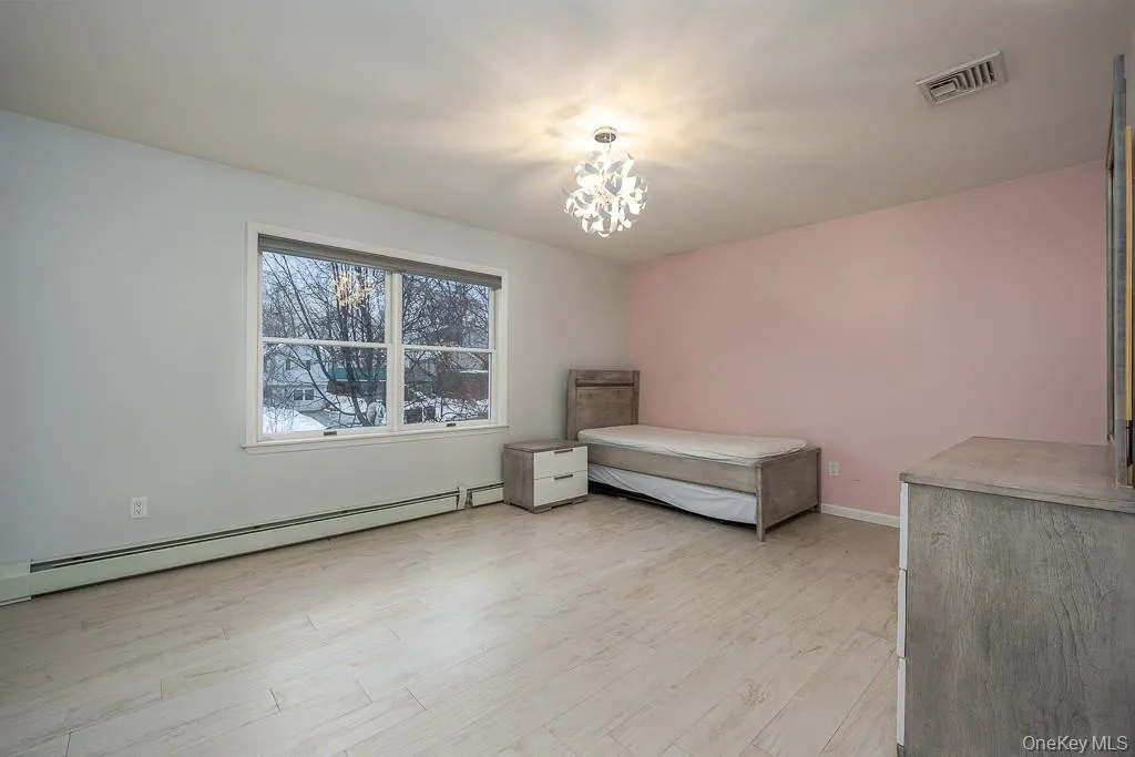 Unfurnished bedroom with a baseboard radiator, light wood finished floors, and a chandelier Unfurnished bedroom with a baseboard radiator, light wood finished floors, and a chandelier