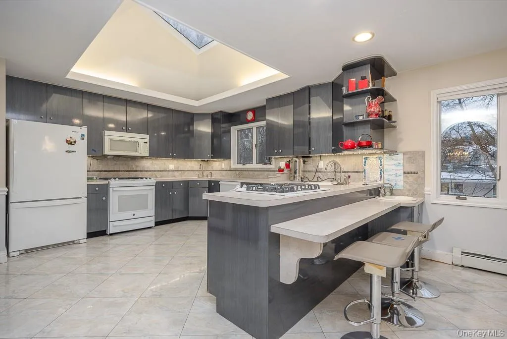 Kitchen with white appliances, a kitchen bar, a skylight, a peninsula, and light countertops Kitchen with white appliances, a kitchen bar, a skylight, a peninsula, and light countertops