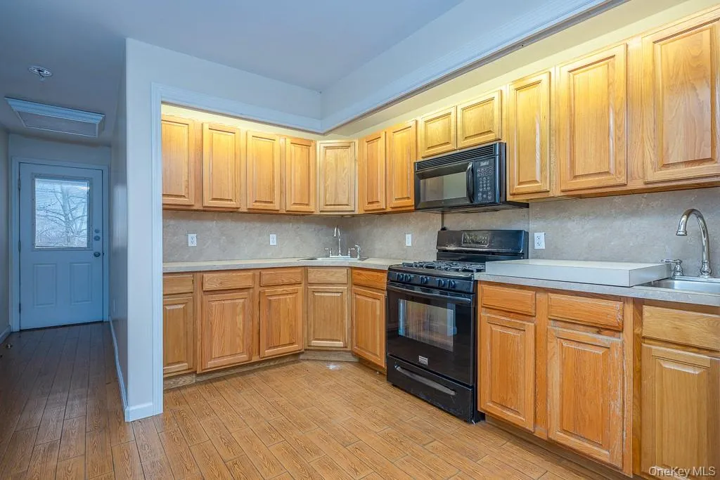 Kitchen with black appliances, light countertops, light wood-style flooring, backsplash, and brown cabinetry Kitchen with black appliances, light countertops, light wood-style flooring, backsplash, and brown cabinetry