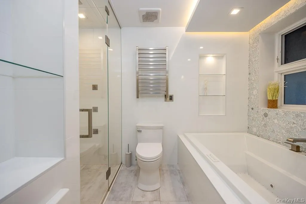 Full bath with a towel warmer, radiator, tile walls, a shower stall, and a garden tub Full bath with a towel warmer, radiator, tile walls, a shower stall, and a garden tub