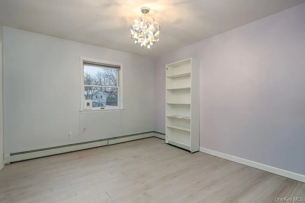 Empty room featuring light wood-style flooring, a baseboard radiator, and a chandelier Empty room featuring light wood-style flooring, a baseboard radiator, and a chandelier