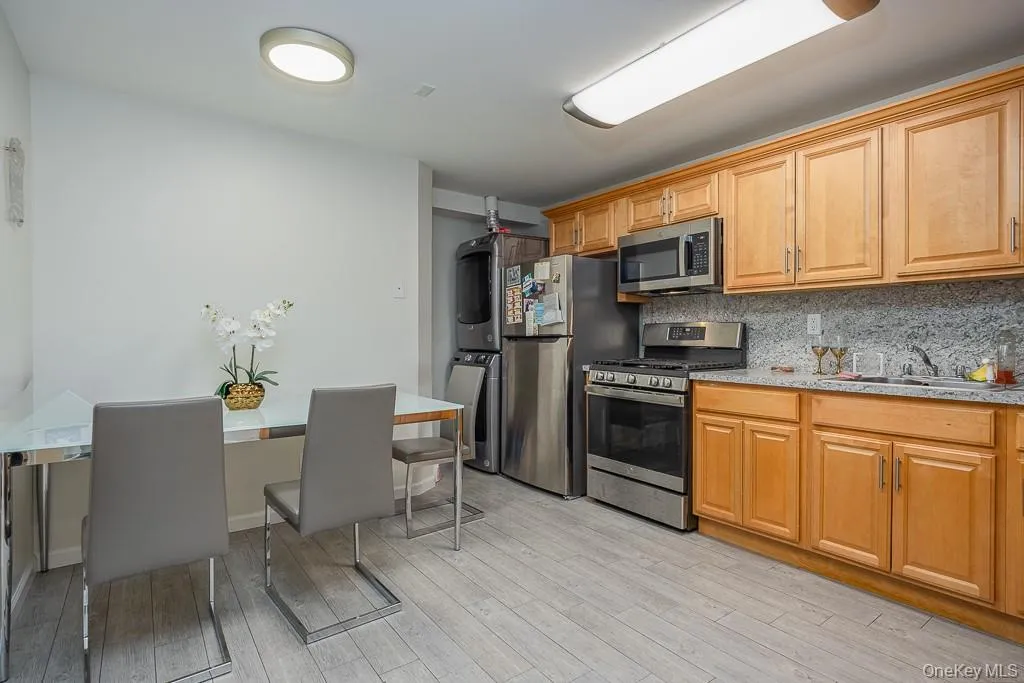 Kitchen featuring appliances with stainless steel finishes, estacked washer and dryer, light wood-style flooring, decorative backsplash, and light stone counters Kitchen featuring appliances with stainless steel finishes, estacked washer and dryer, light wood-style flooring, decorative backsplash, and light stone counters