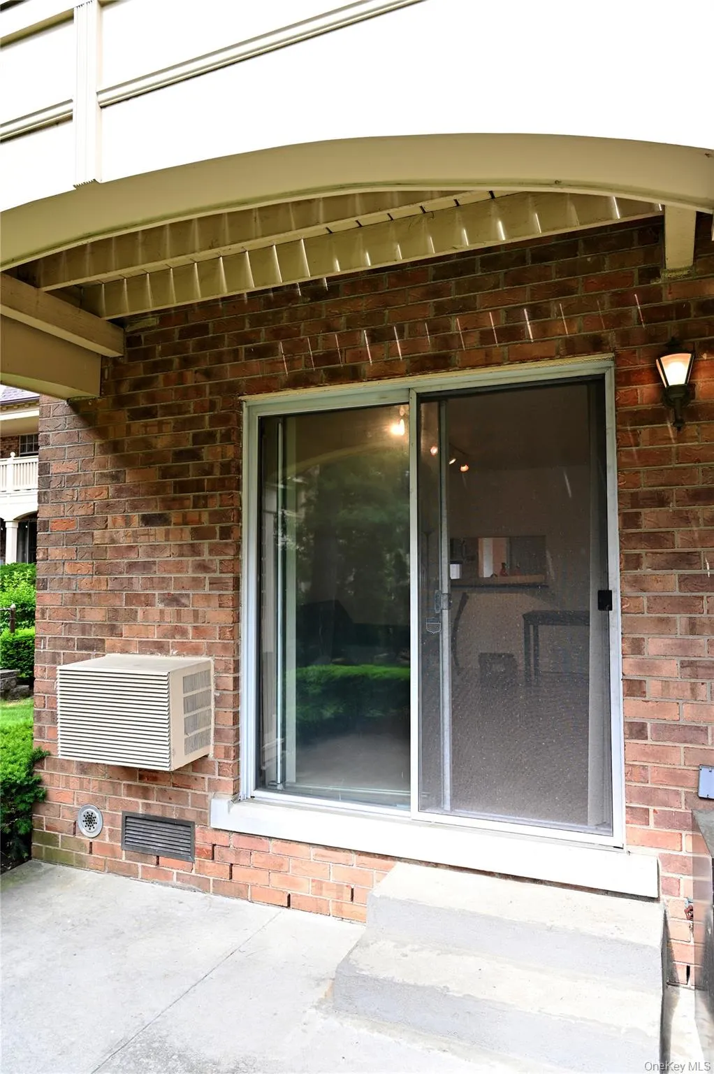 Brick exterior featuring a sliding glass door with screen, concrete patio, and window-mounted air conditioning unit Brick exterior featuring a sliding glass door with screen, concrete patio, and window-mounted air conditioning unit