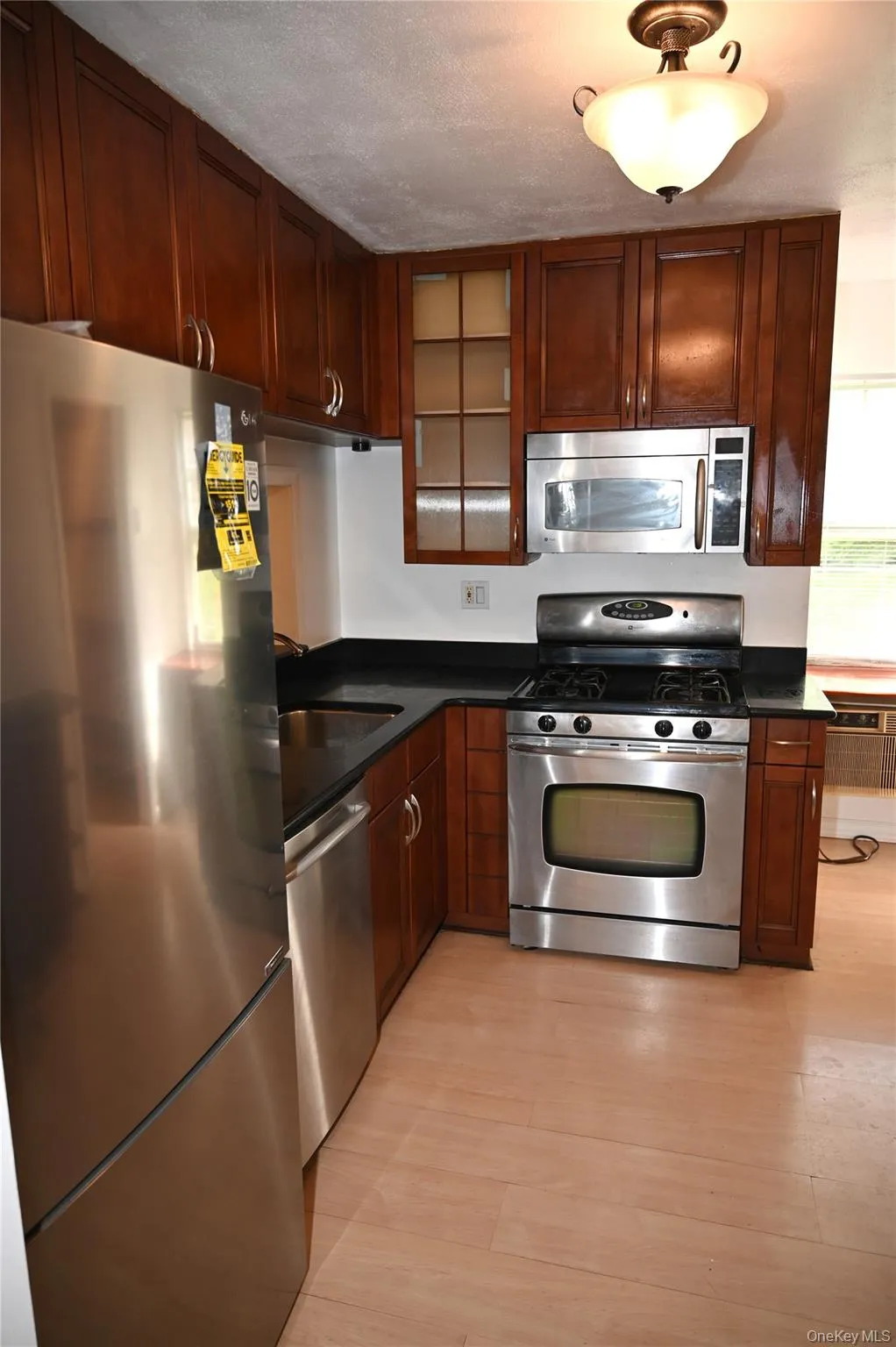 Kitchen featuring wood-finish cabinetry, black countertops, and stainless steel appliances including a refrigerator, dishwasher, range, and microwave Kitchen featuring wood-finish cabinetry, black countertops, and stainless steel appliances including a refrigerator, dishwasher, range, and microwave