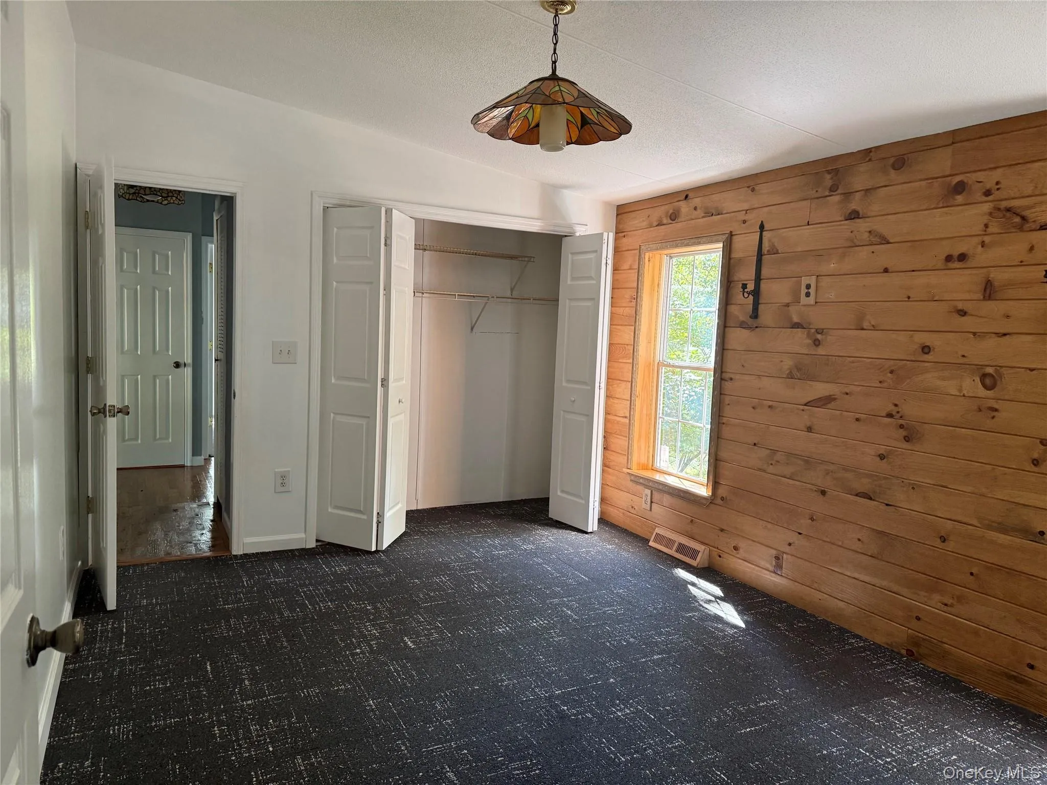 Unfurnished bedroom with wood walls, a closet, and dark carpet Unfurnished bedroom with wood walls, a closet, and dark carpet