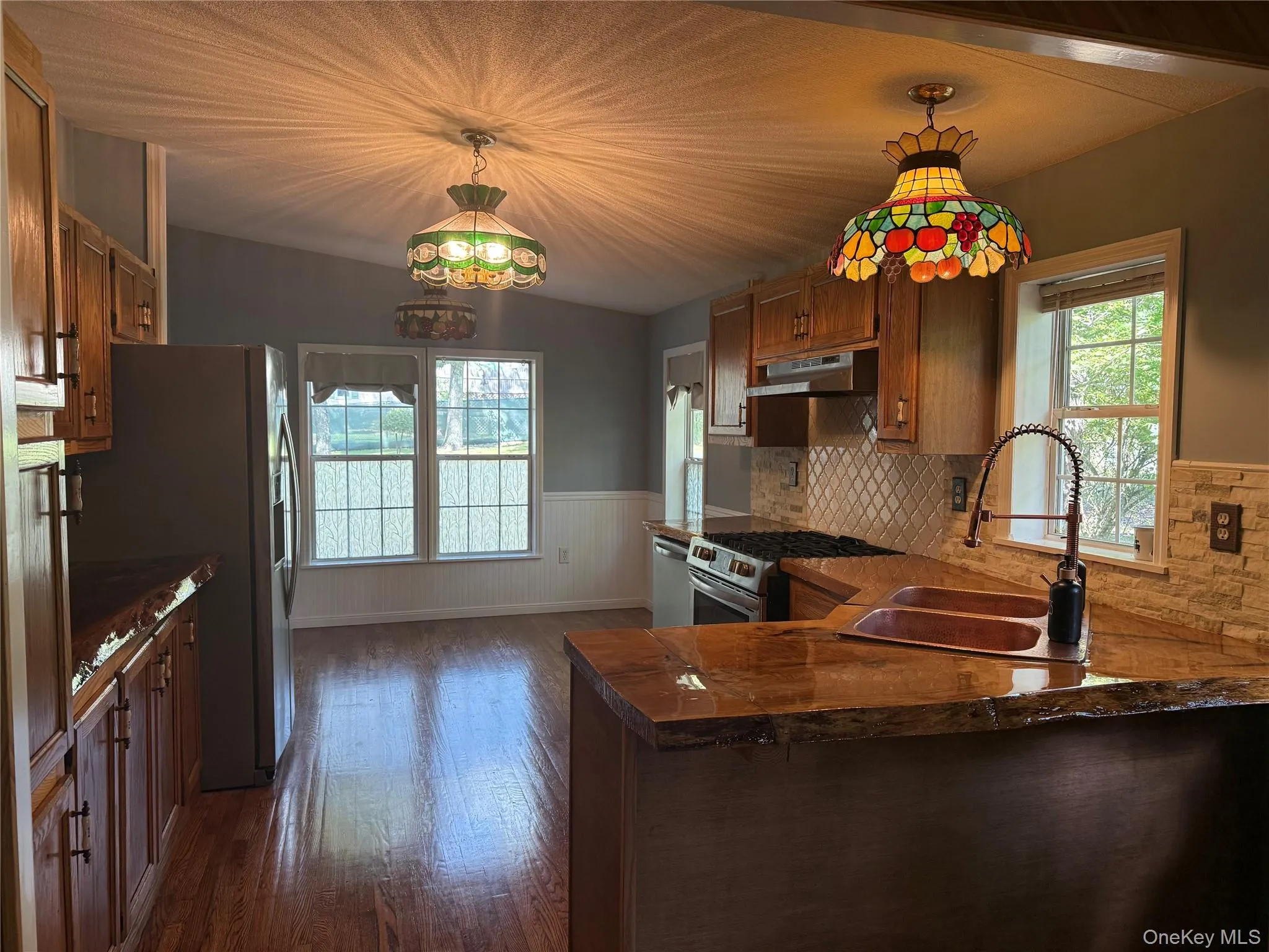 Kitchen with dark wood-style floors, brown cabinets, hanging light fixtures, stainless steel appliances, and a wainscoted wall Kitchen with dark wood-style floors, brown cabinets, hanging light fixtures, stainless steel appliances, and a wainscoted wall