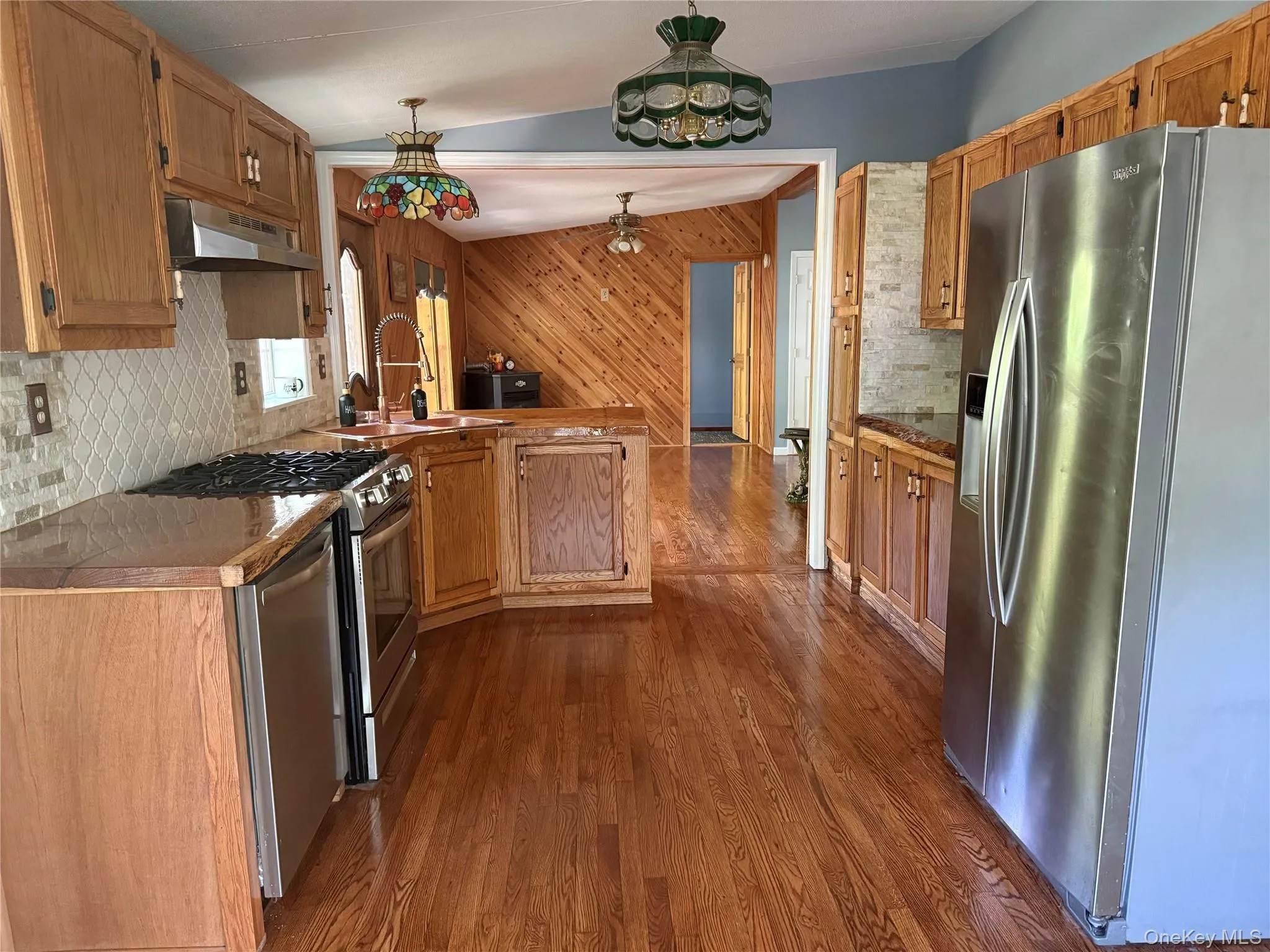 Kitchen with backsplash, stainless steel appliances, dark wood-style floors, under cabinet range hood, and decorative light fixtures Kitchen with backsplash, stainless steel appliances, dark wood-style floors, under cabinet range hood, and decorative light fixtures