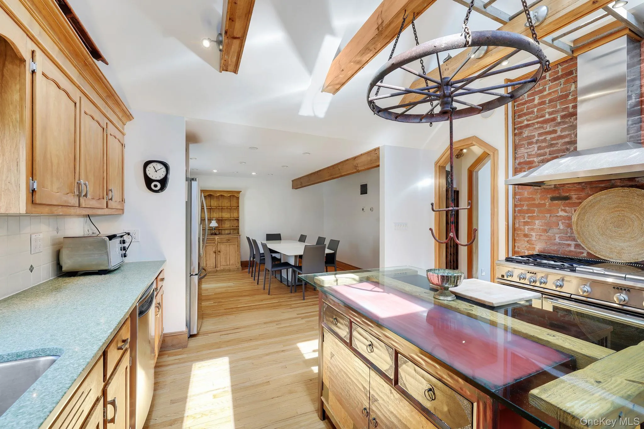 Kitchen featuring a Wolf gas cooktop and electric oven, exposed brick backsplash, and a custom made central island with a glass countertop. Kitchen featuring a Wolf gas cooktop and electric oven, exposed brick backsplash, and a custom made central island with a glass countertop.