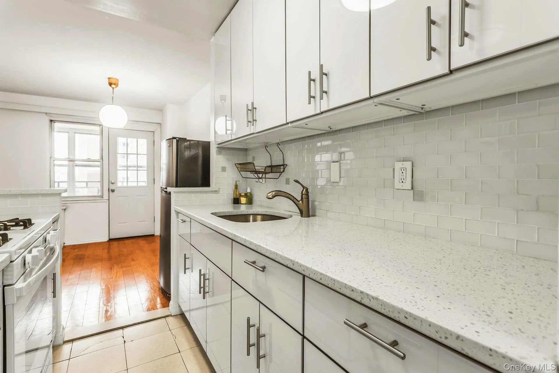 Kitchen with decorative light fixtures, light stone countertops, white gas range oven, white cabinetry, and tasteful backsplash Kitchen with decorative light fixtures, light stone countertops, white gas range oven, white cabinetry, and tasteful backsplash