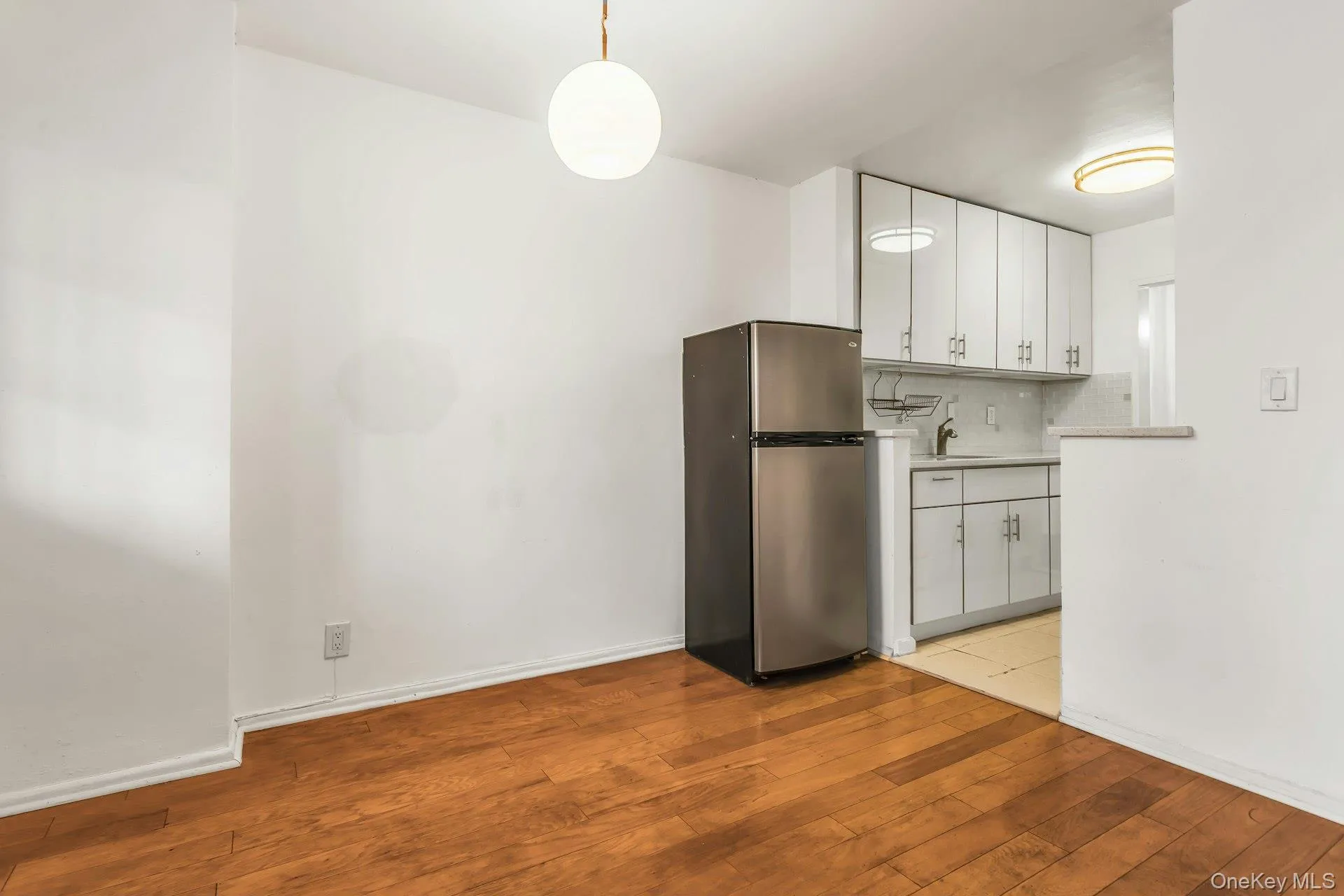 Kitchen featuring white cabinetry, freestanding refrigerator, light countertops, decorative backsplash, and pendant lighting Kitchen featuring white cabinetry, freestanding refrigerator, light countertops, decorative backsplash, and pendant lighting
