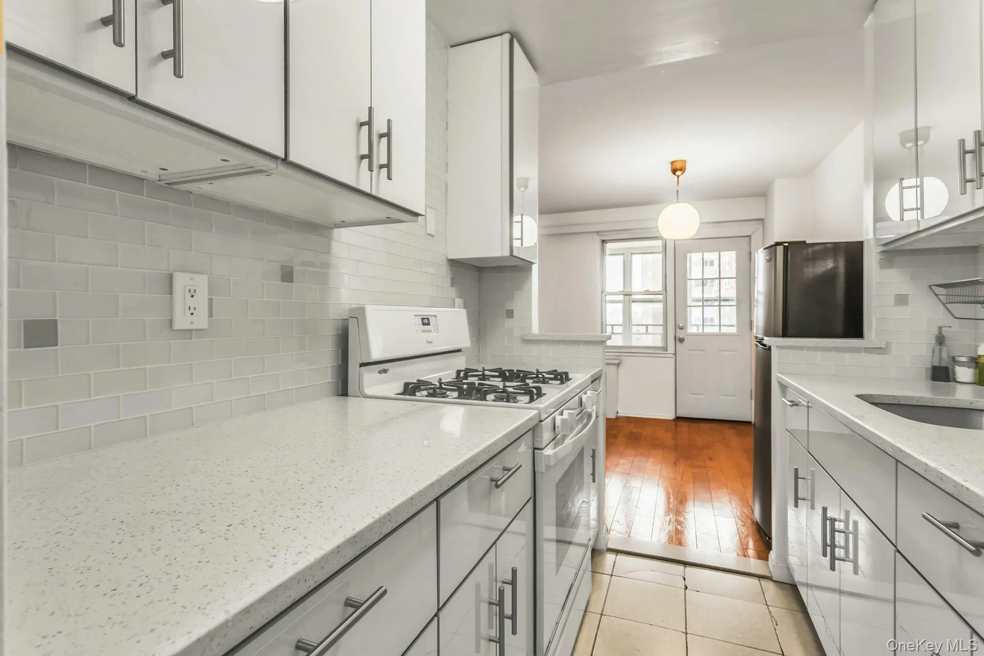Kitchen featuring white gas stove, freestanding refrigerator, light stone countertops, pendant lighting, and backsplash Kitchen featuring white gas stove, freestanding refrigerator, light stone countertops, pendant lighting, and backsplash