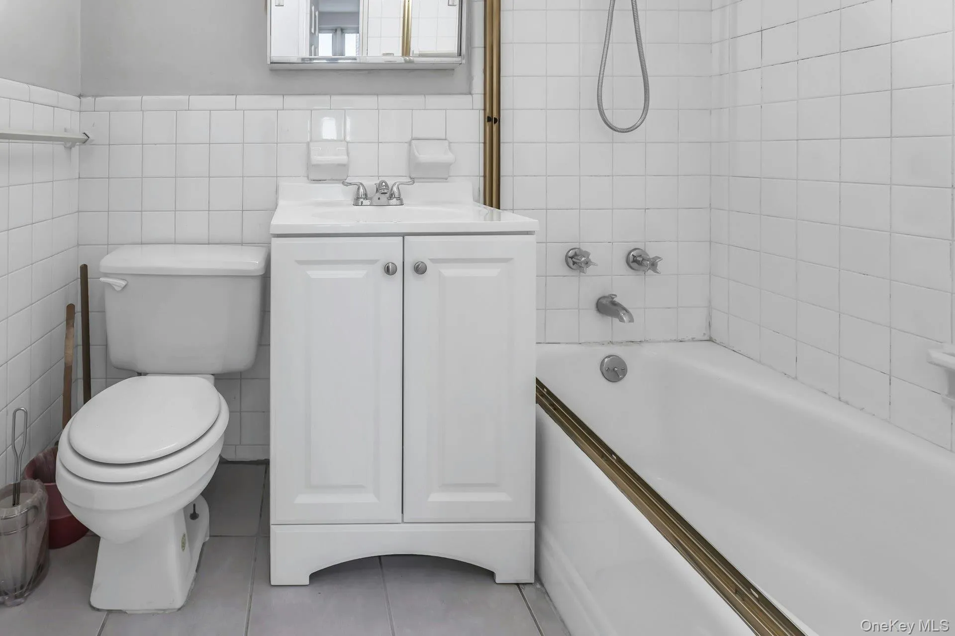 Full bathroom with tile walls, bathtub / shower combination, vanity, a wainscoted wall, and light tile patterned floors Full bathroom with tile walls, bathtub / shower combination, vanity, a wainscoted wall, and light tile patterned floors