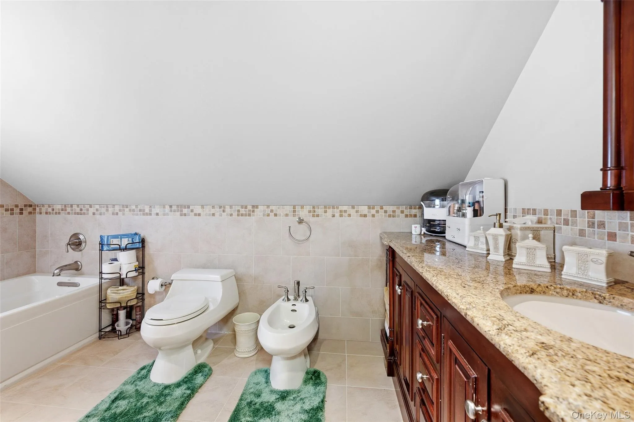 En-suite bathroom featuring a built-in tub, tiled walls, a toilet, and a bidet En-suite bathroom featuring a built-in tub, tiled walls, a toilet, and a bidet