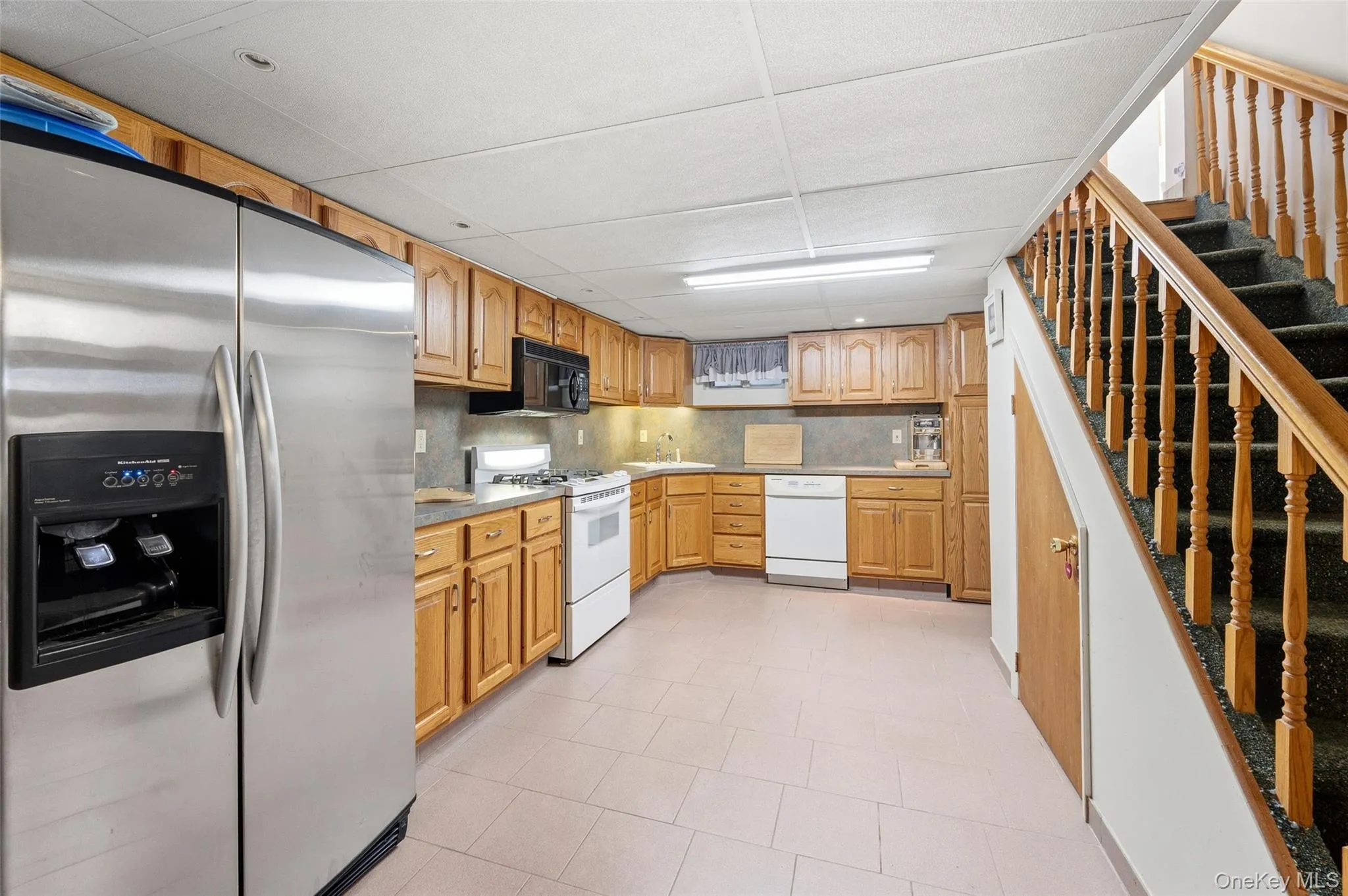 Full kitchen featuring wood cabinetry, stainless steel refrigerator, white range, white dishwasher, and tile flooring Full kitchen featuring wood cabinetry, stainless steel refrigerator, white range, white dishwasher, and tile flooring