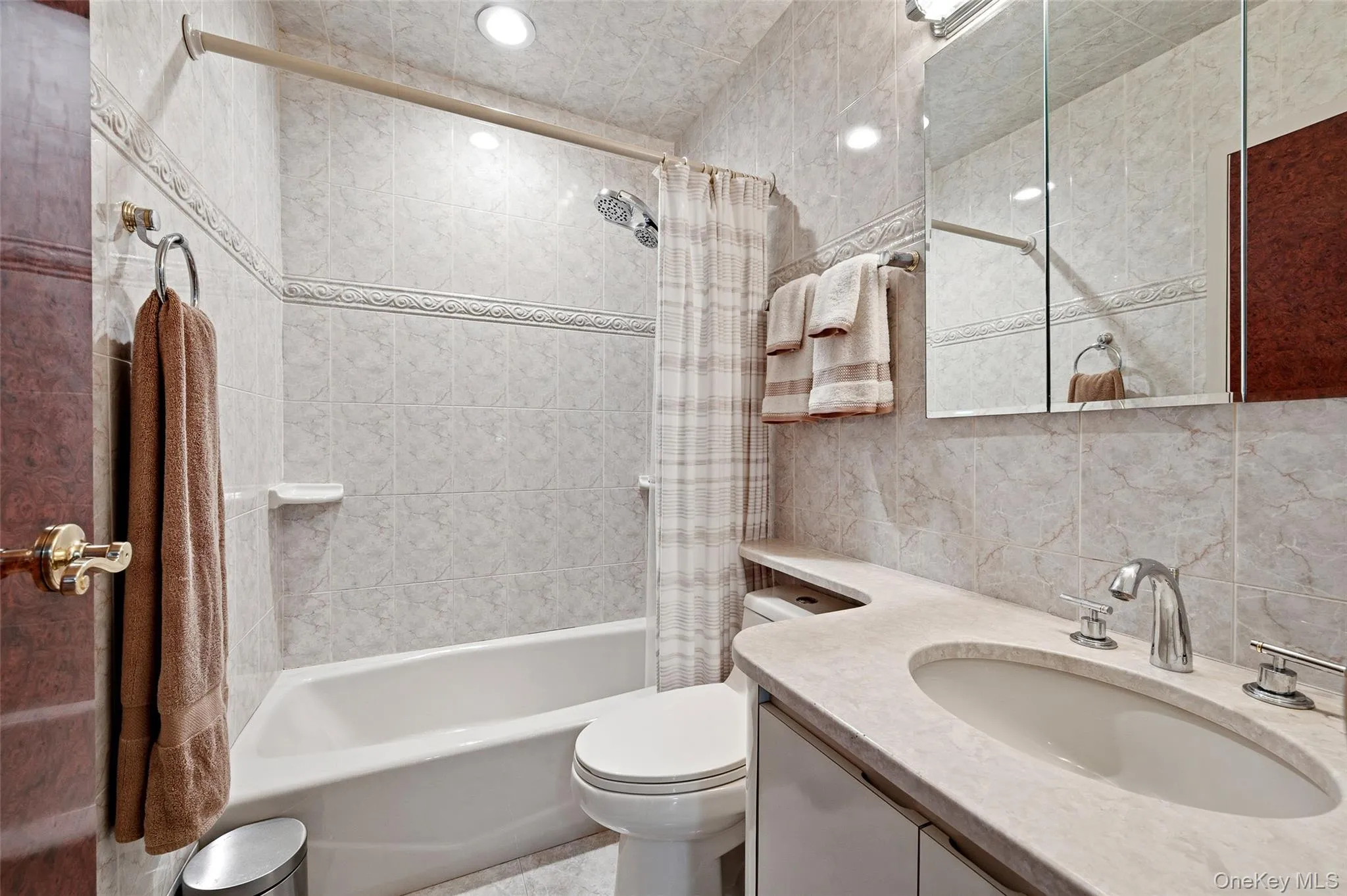 Bathroom featuring a tub and shower combination with tiled surround, an integrated vanity sink with dual-handle faucet, recessed lighting, and a mirrored medicine cabinet Bathroom featuring a tub and shower combination with tiled surround, an integrated vanity sink with dual-handle faucet, recessed lighting, and a mirrored medicine cabinet
