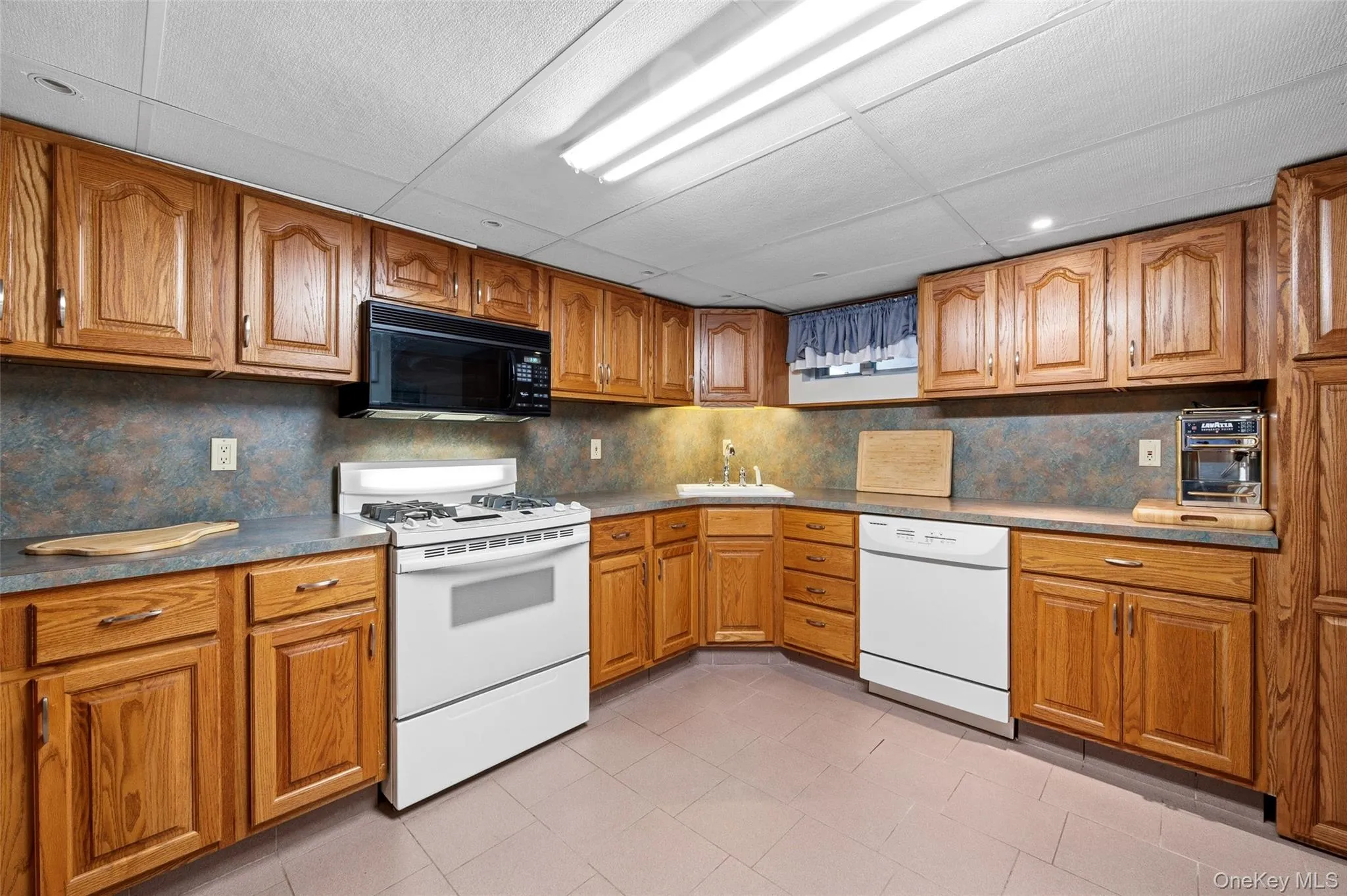Kitchen featuring extensive wood cabinetry, L-shaped countertops, a white gas range, a black built-in microwave, and a white dishwasher Kitchen featuring extensive wood cabinetry, L-shaped countertops, a white gas range, a black built-in microwave, and a white dishwasher