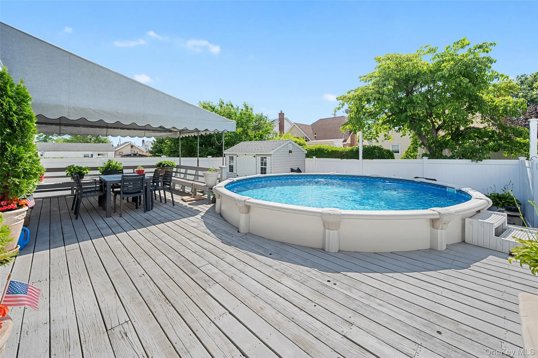 Expansive wood-finish deck featuring an above-ground pool with integrated steps, a white privacy fence, and a dedicated shaded dining area Expansive wood-finish deck featuring an above-ground pool with integrated steps, a white privacy fence, and a dedicated shaded dining area