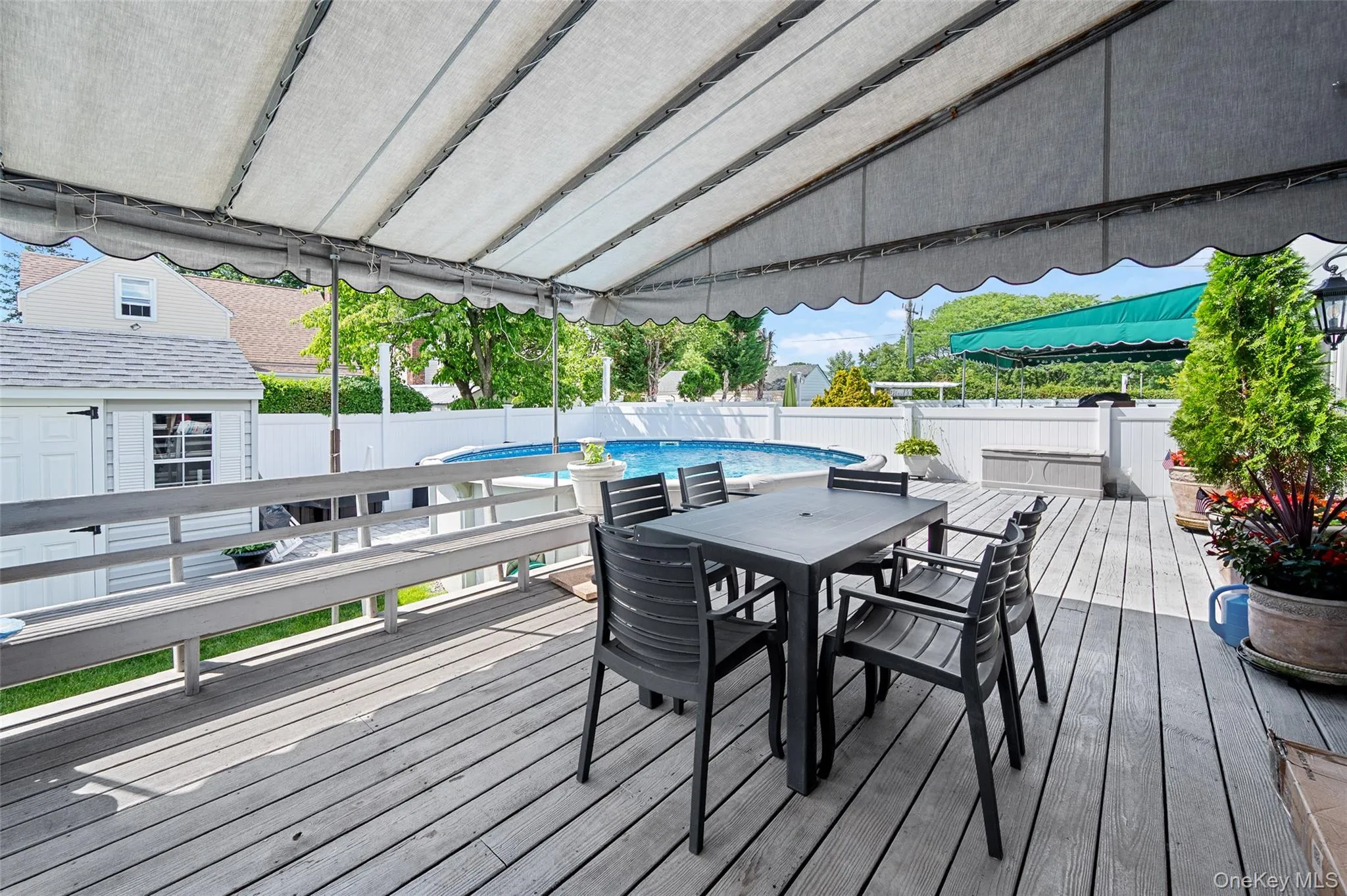 Expansive wood deck with a retractable awning, integrated bench seating, and an above-ground swimming pool Expansive wood deck with a retractable awning, integrated bench seating, and an above-ground swimming pool
